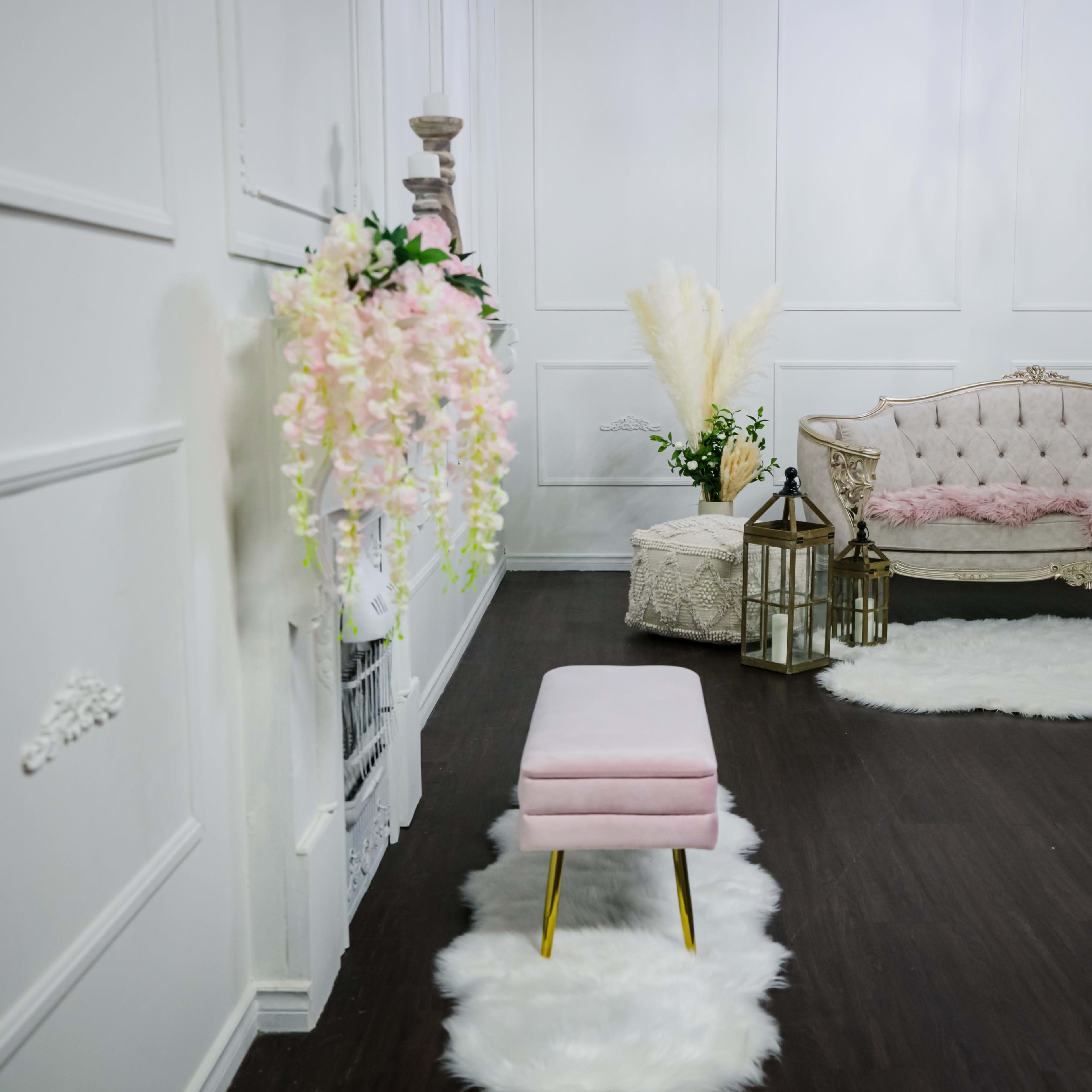A decorated room with a pink sofa, a matching stool, and a white fluffy rug on a dark wooden floor.