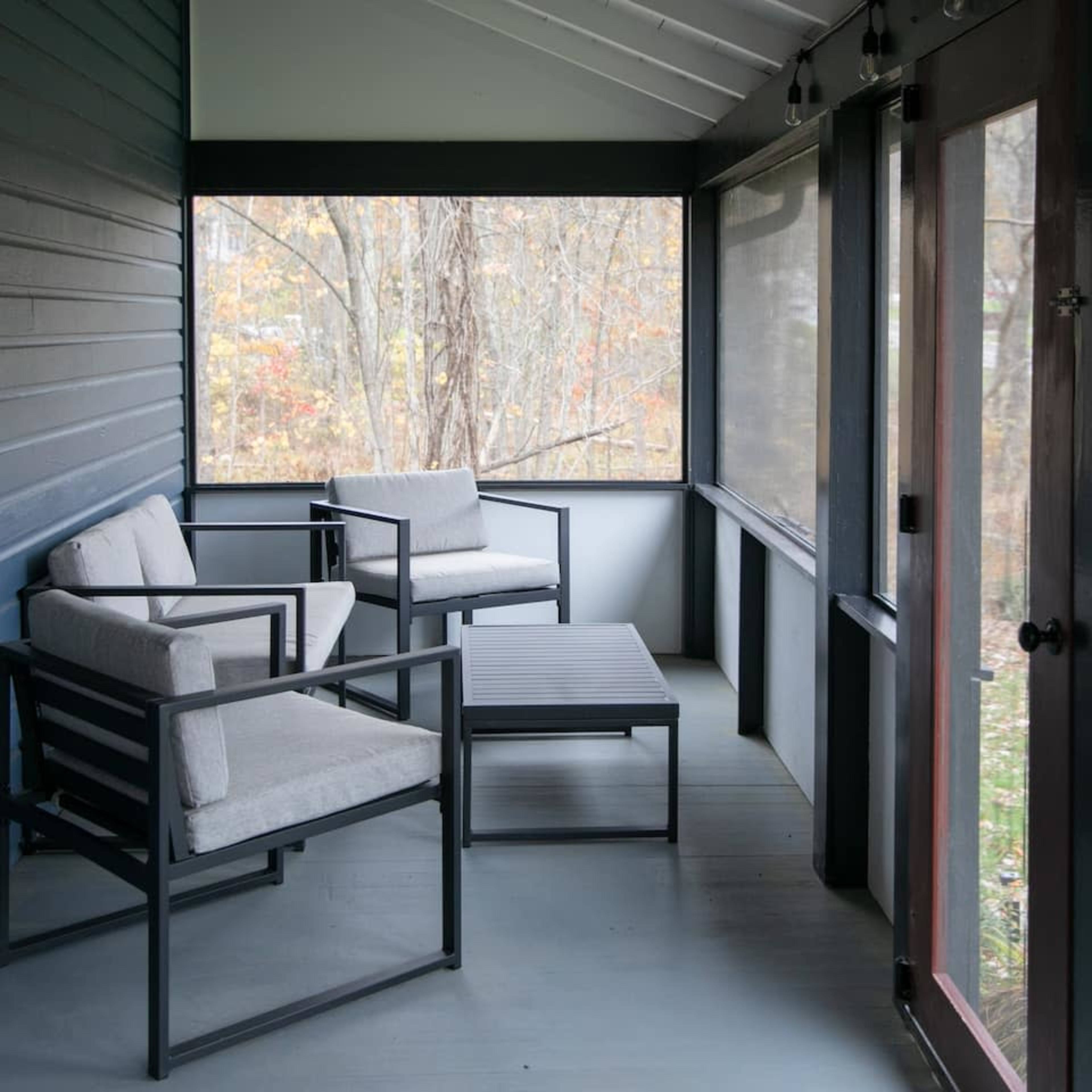 A screened-in porch featuring two gray chairs and a small table on a wooden floor.