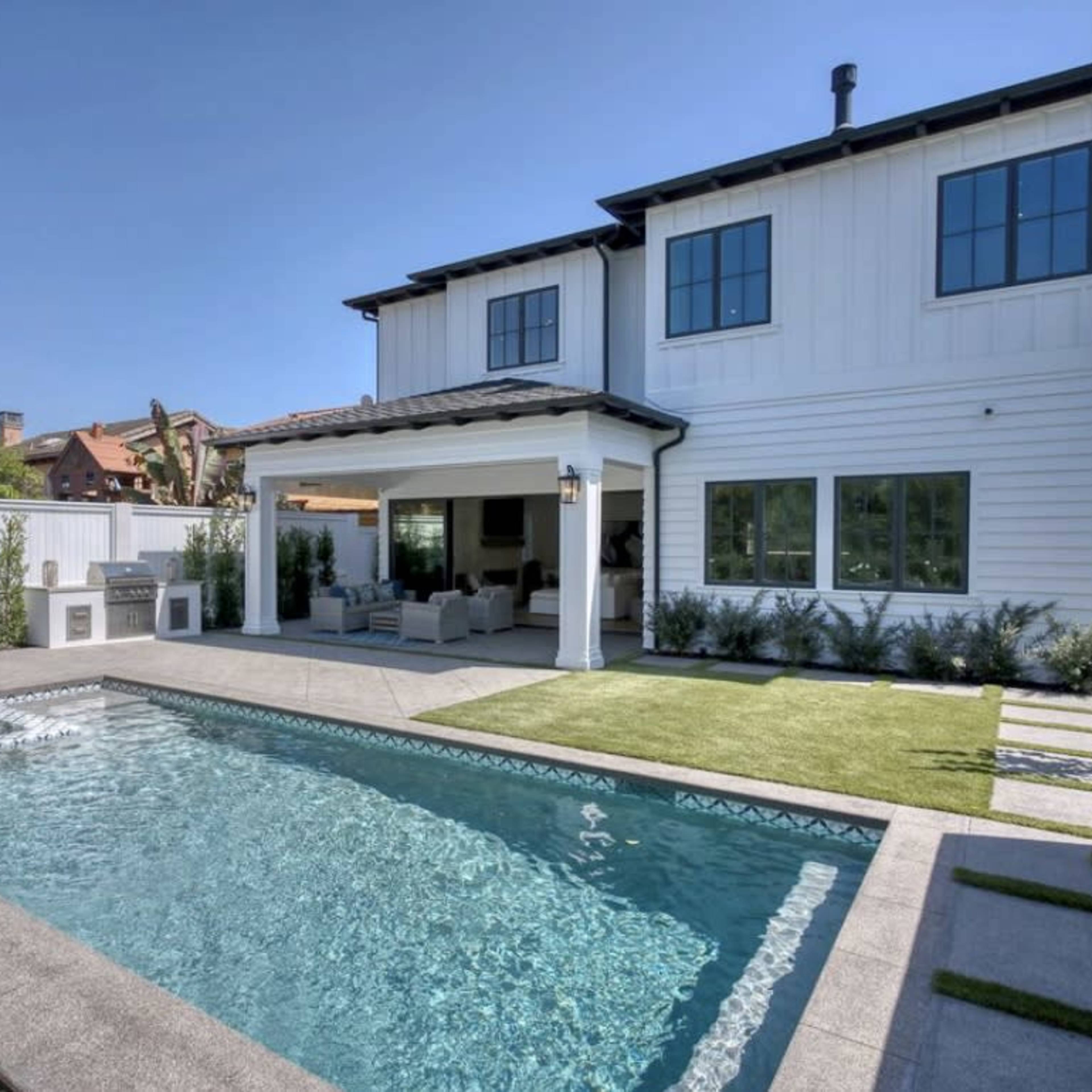 A modern two-story house with a swimming pool surrounded by a landscaped yard and patio area.
