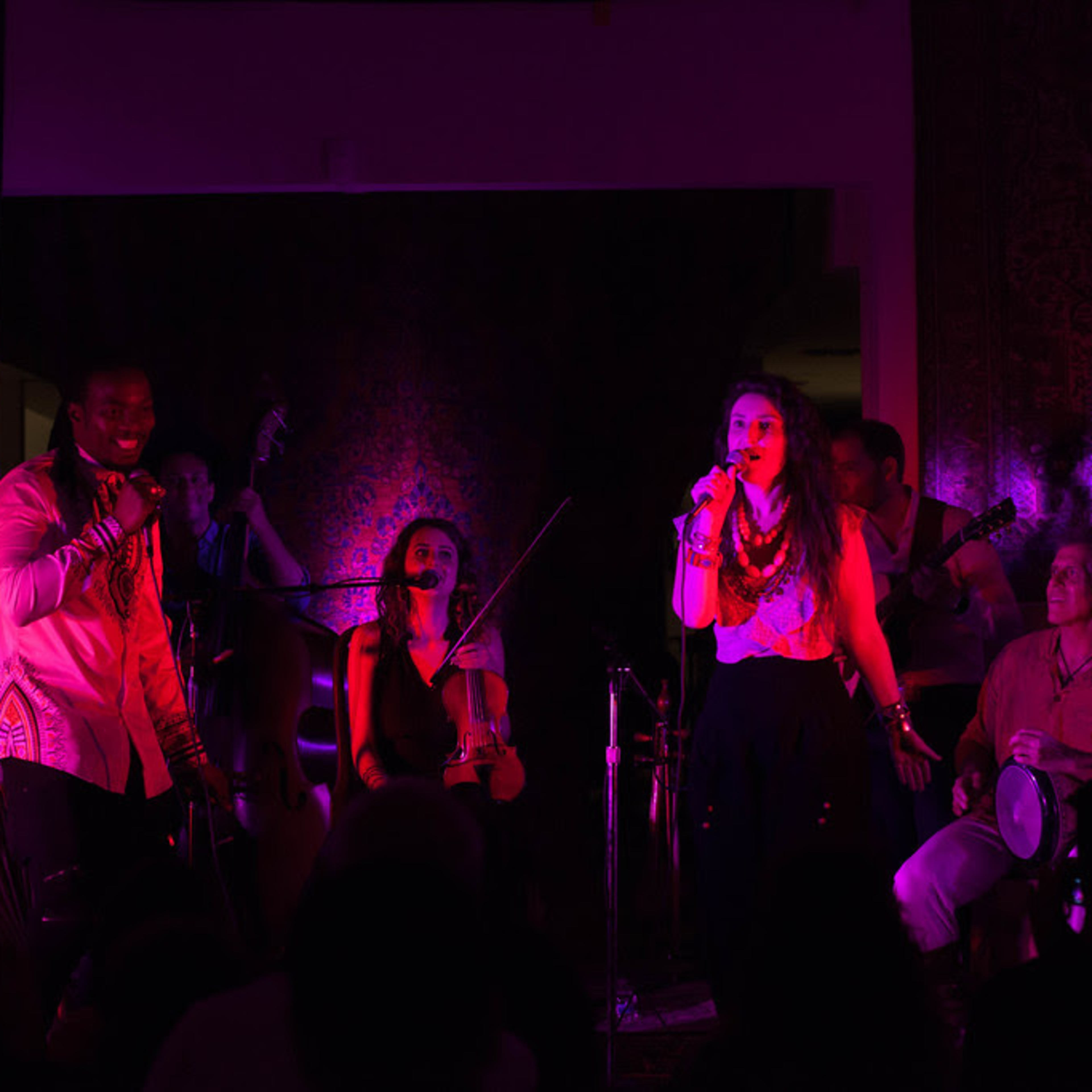 A diverse group of musicians performs on stage with colorful lights illuminating the scene.