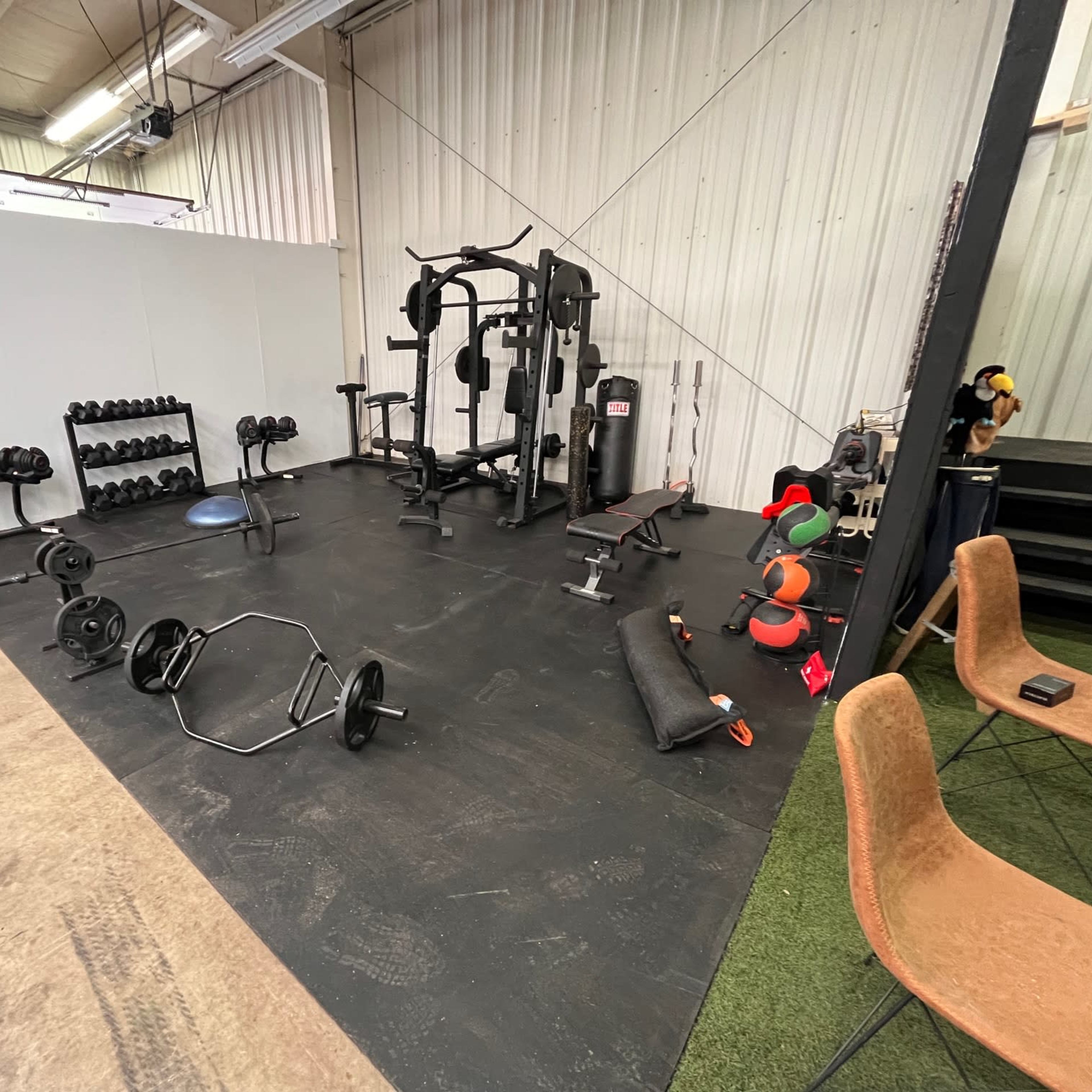 A gym area with various weights, a squat rack, and workout benches, surrounded by a spacious, industrial-style interior.