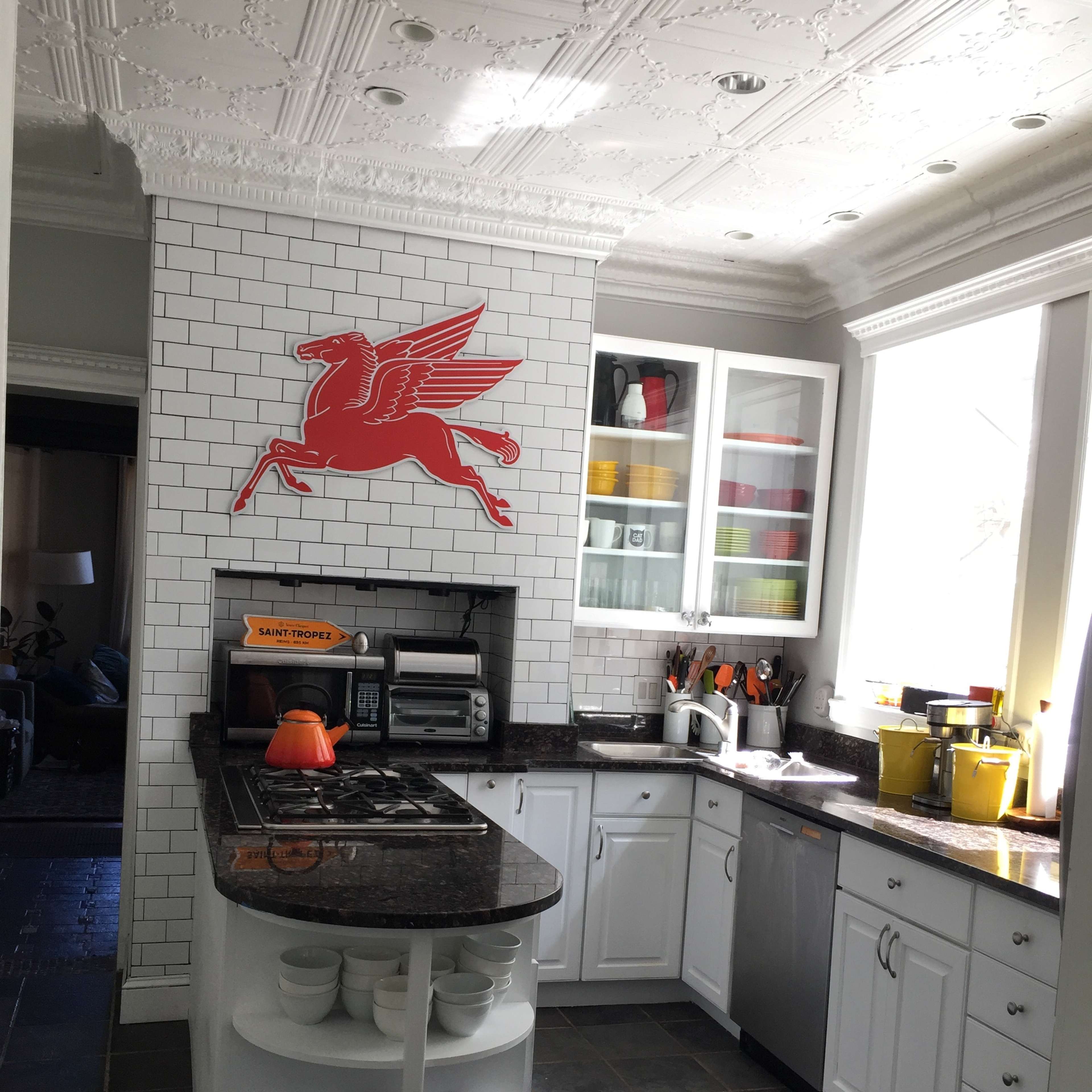 A kitchen with white cabinetry, black countertops, a tiled backsplash, and a prominently displayed red Pegasus logo on the wall.