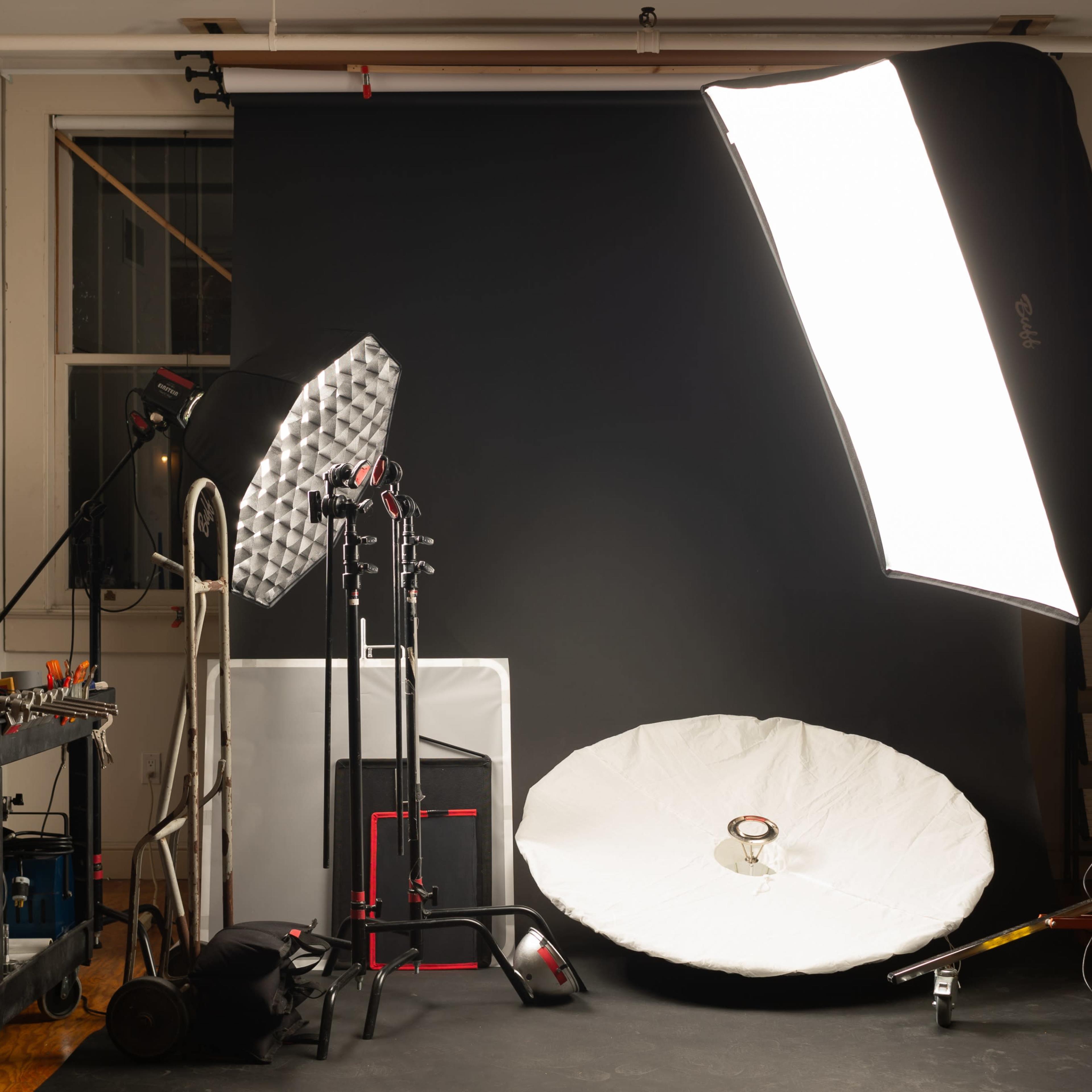 A photography studio setup with various lighting equipment, including softboxes and stands, against a black backdrop.