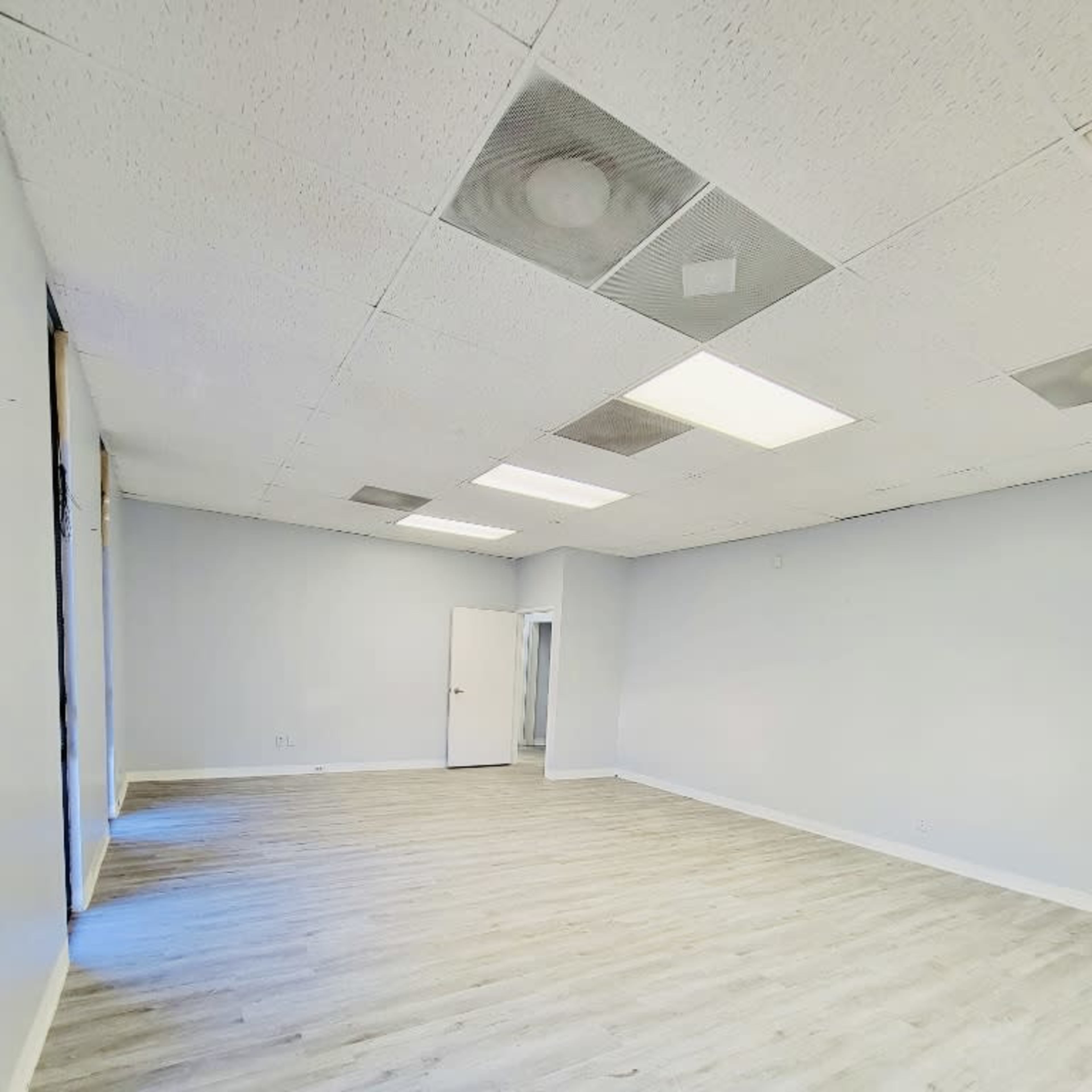 A vacant room with light-colored walls, a light wooden floor, and several ceiling lights.