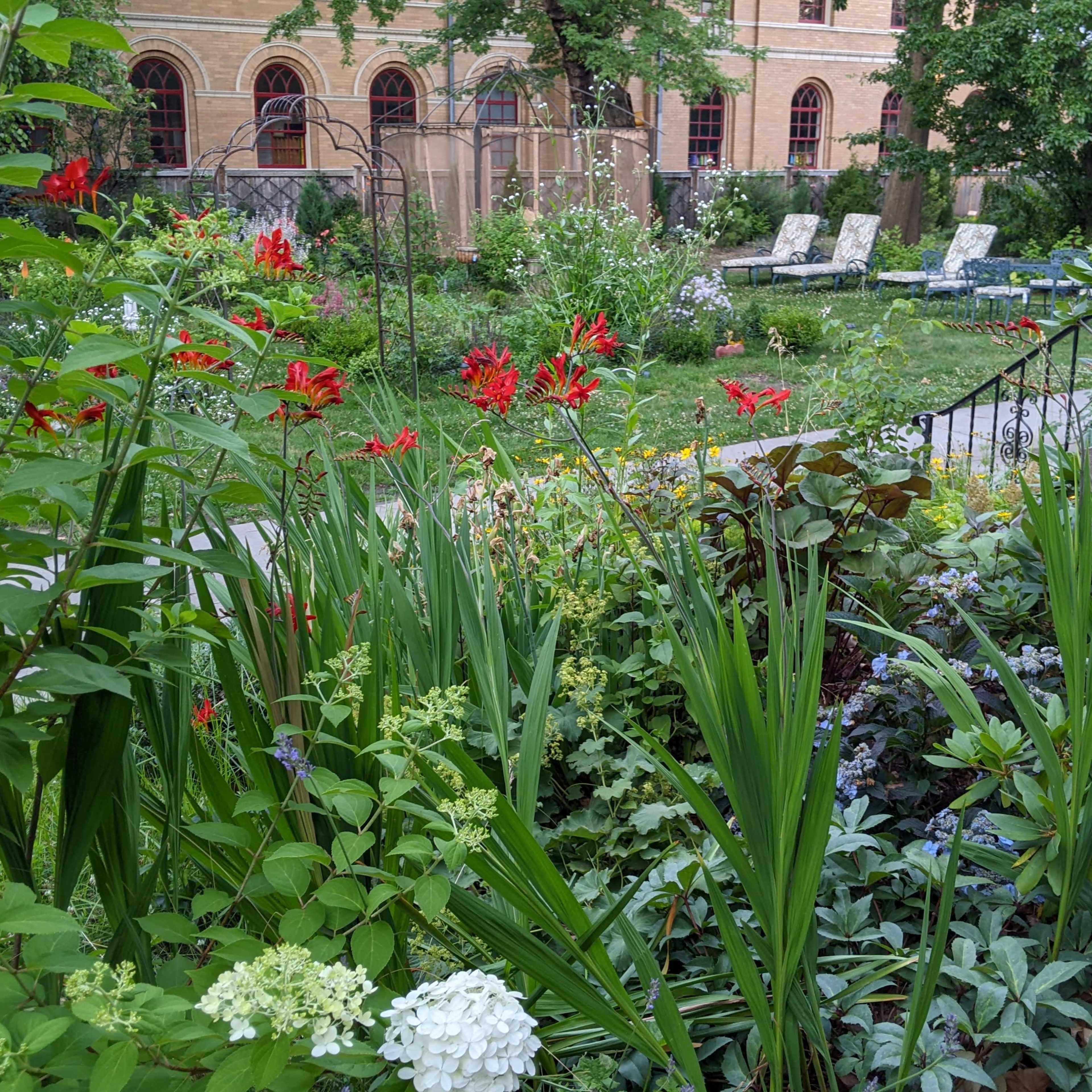 A garden scene features vibrant flowers and lush greenery in front of a historic building with large windows.