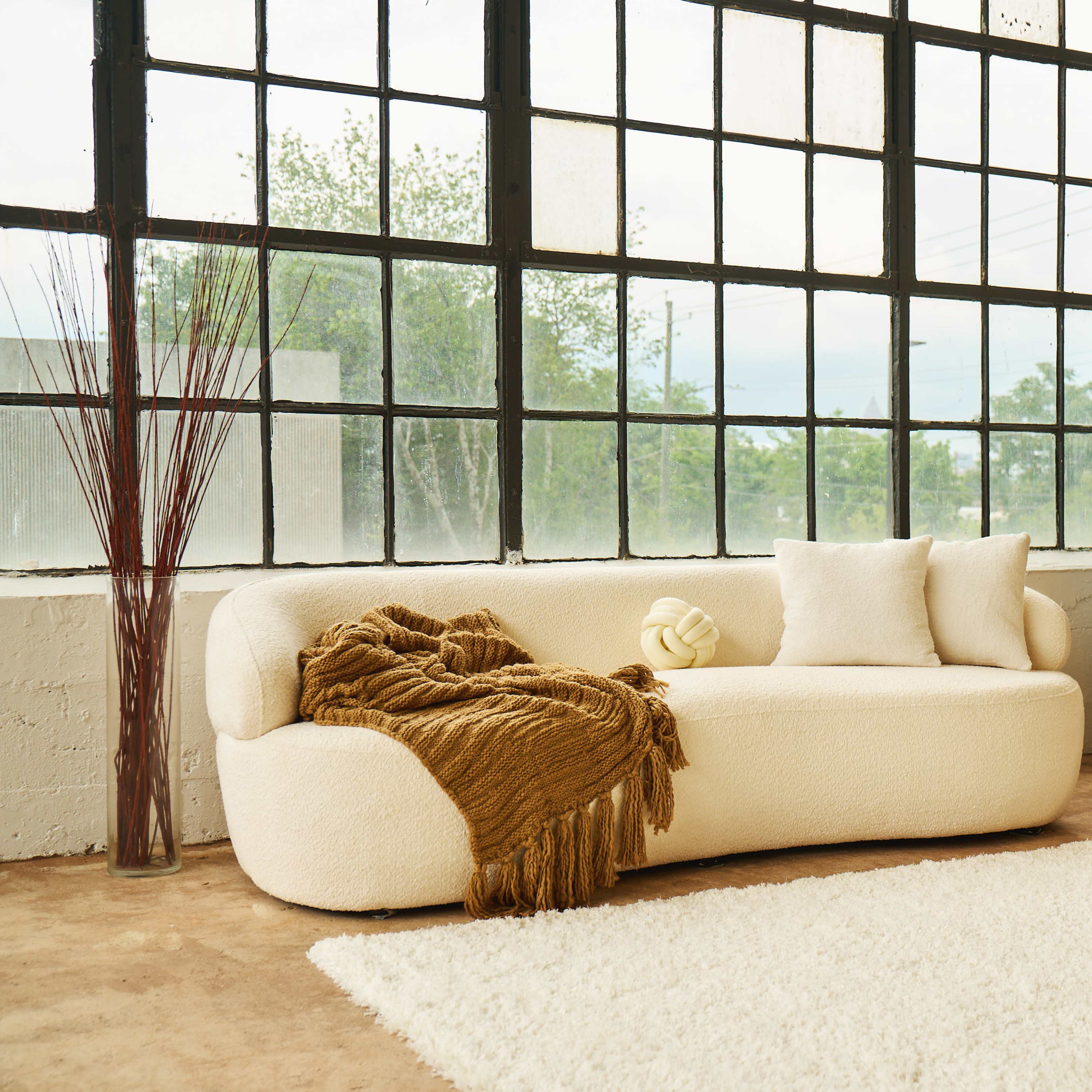A cozy living area featuring a boucle-style sofa, a light-colored armchair, a large mirror, and decorative elements like a vase and a fluffy rug.