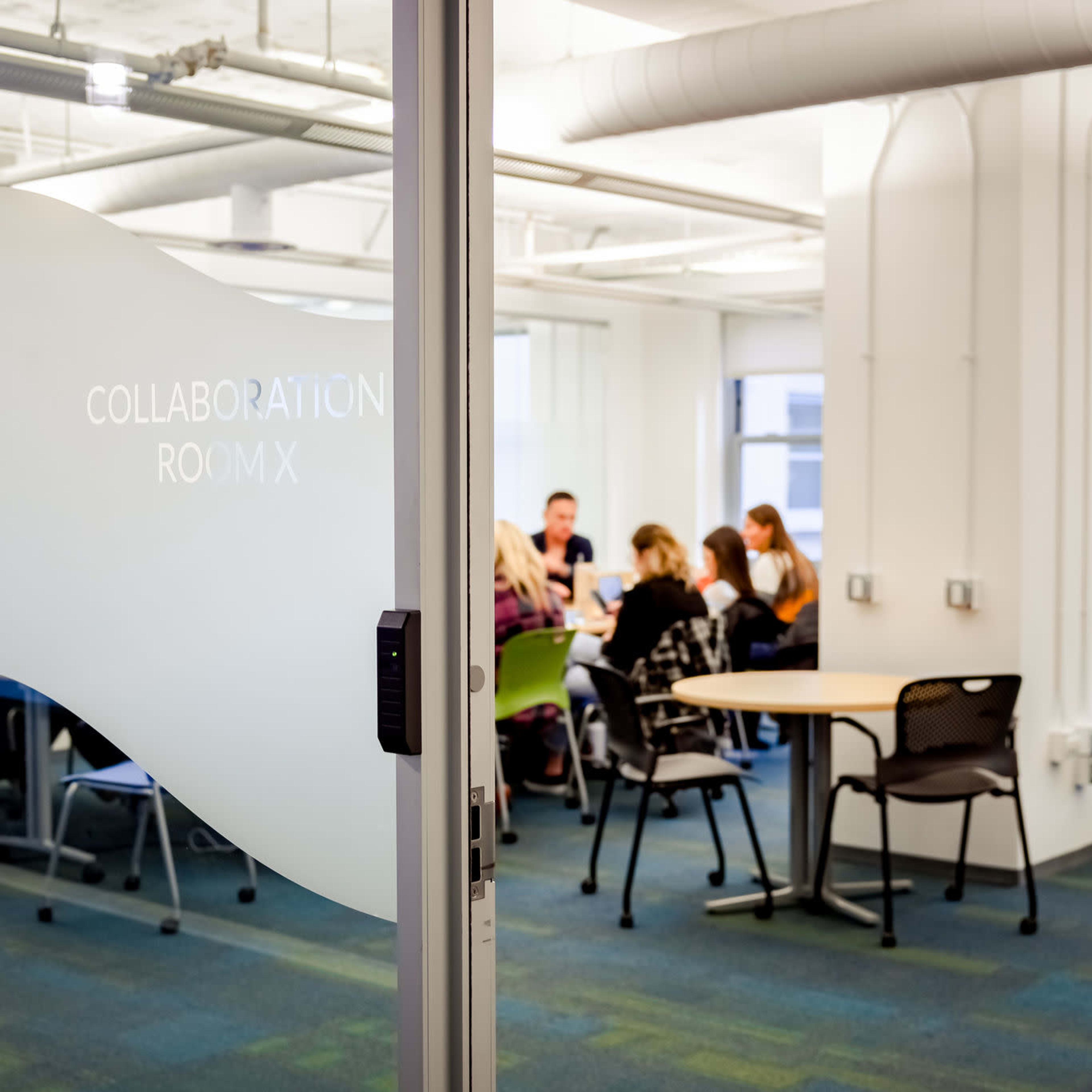 A glass door leading to a collaboration room where a group of people is seated around a table.