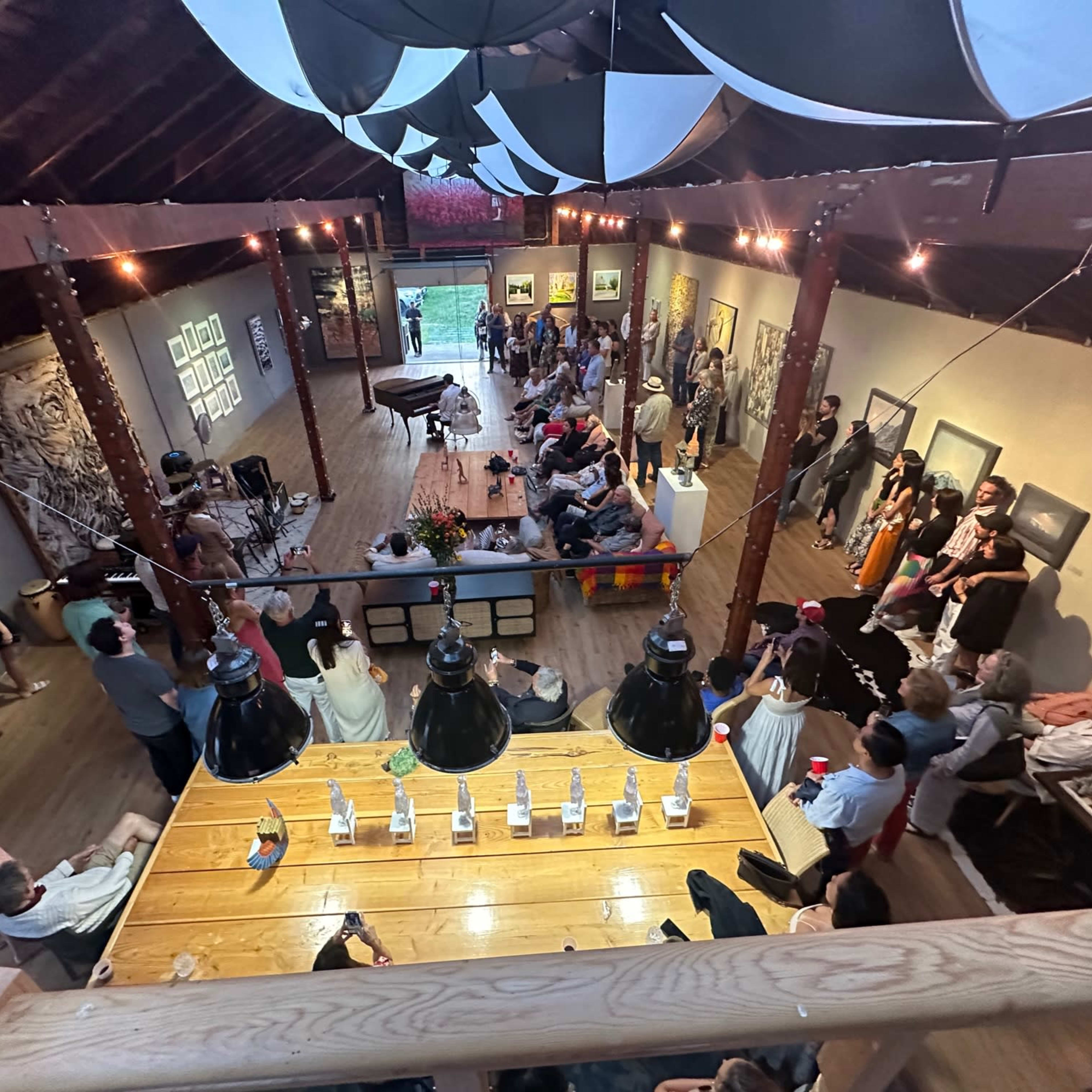 A large gathering of people is taking place in a spacious, modern art setting with high ceilings and artwork displayed on the walls.