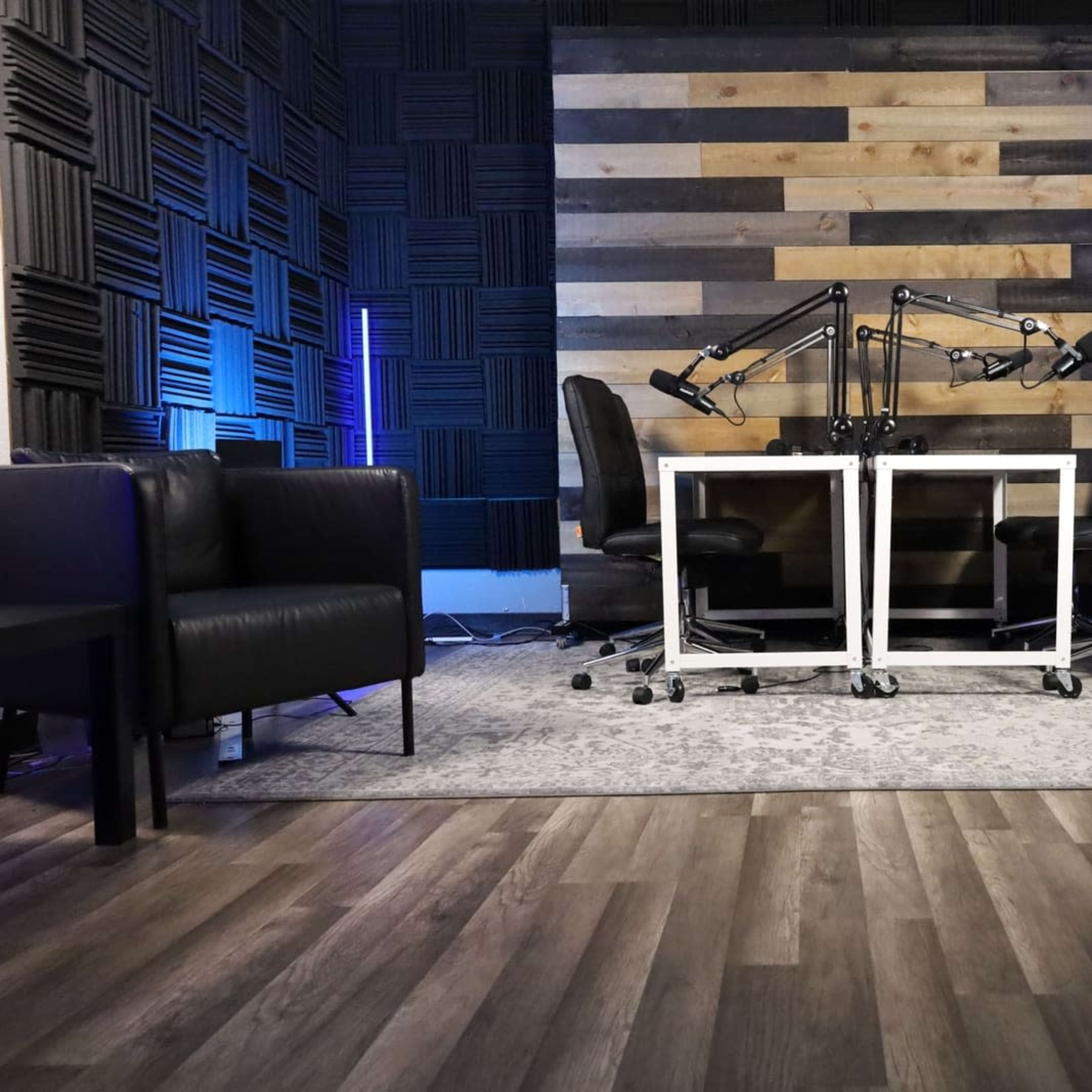 A modern podcast studio with soundproofed walls, two microphone stands positioned over a table, and dark seating arrangements.