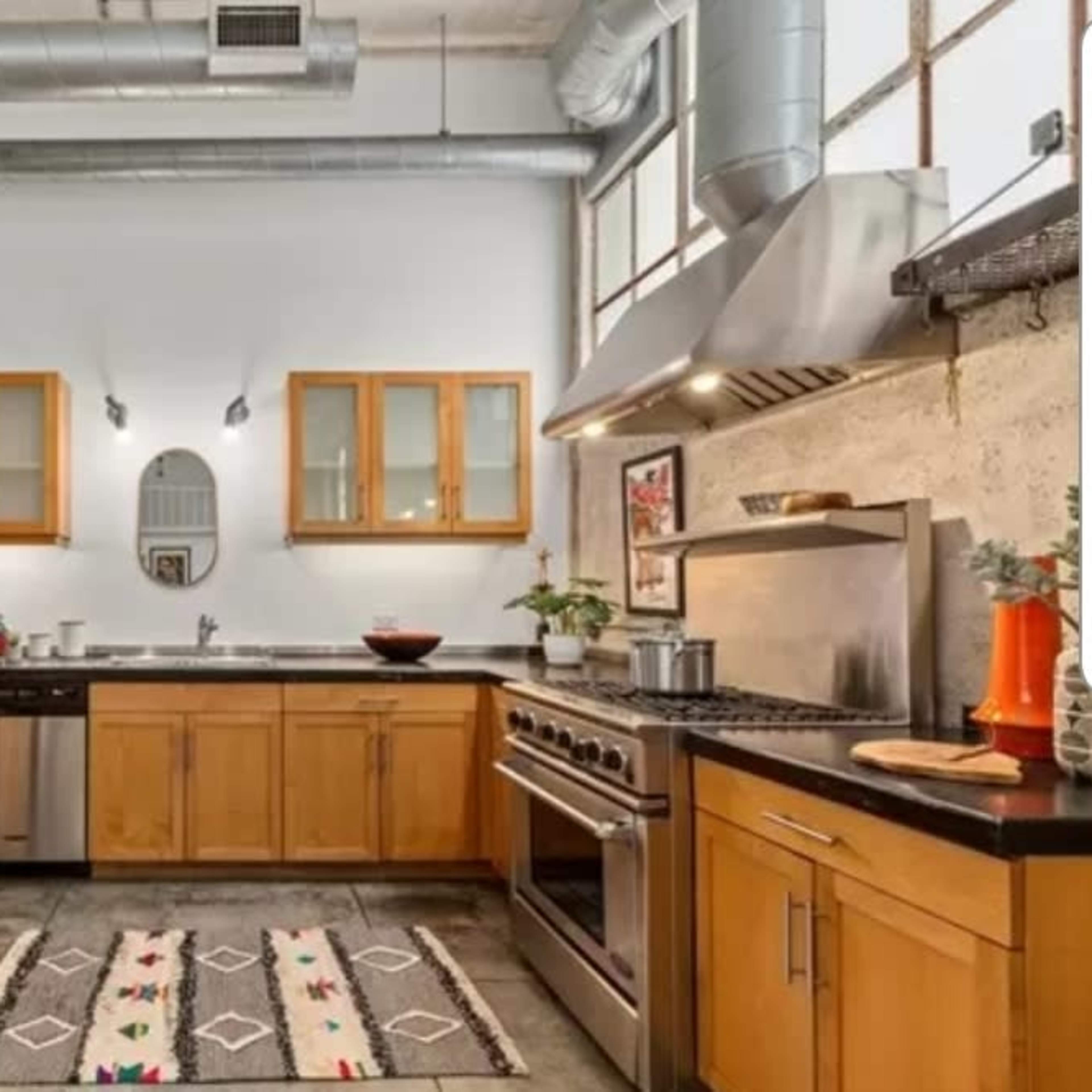This kitchen features wooden cabinets, stainless steel appliances, and a large oven range, with a patterned rug on the floor.