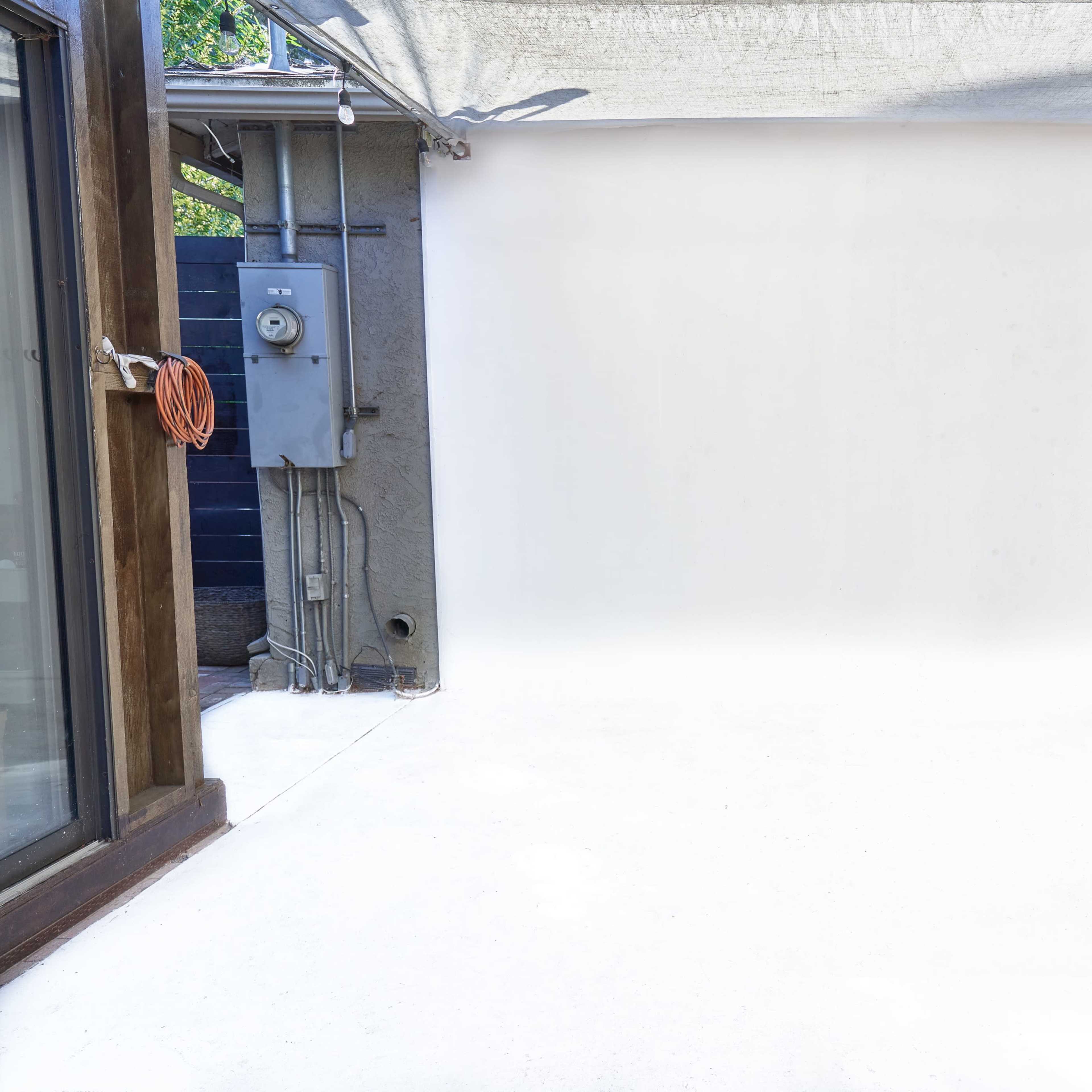 A white backdrop set up in an outdoor space, with one side featuring a door and a power meter on the wall.