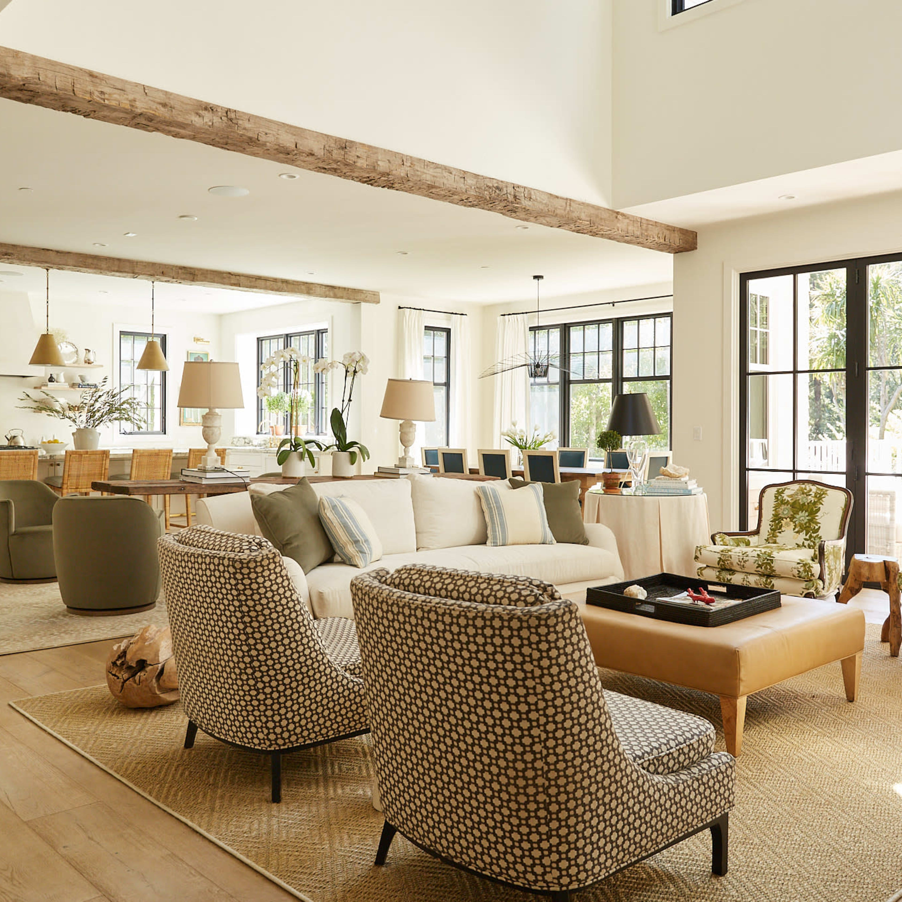 A spacious living area features a mix of modern furniture and natural light, with a large sofa, patterned chairs, and a dining area in the background.