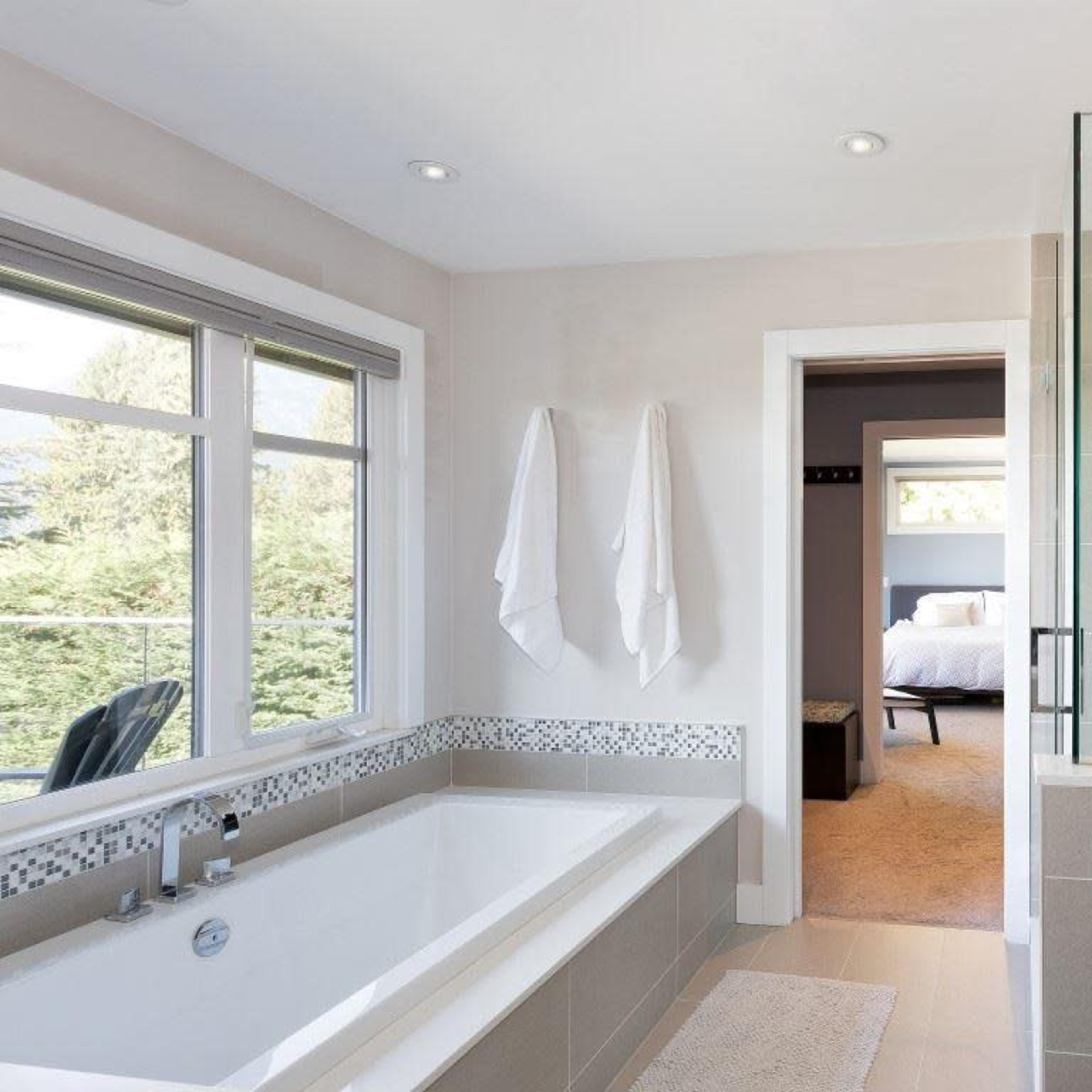 A modern bathroom with a freestanding bathtub, a glass shower enclosure, and two white towels hanging on the wall.