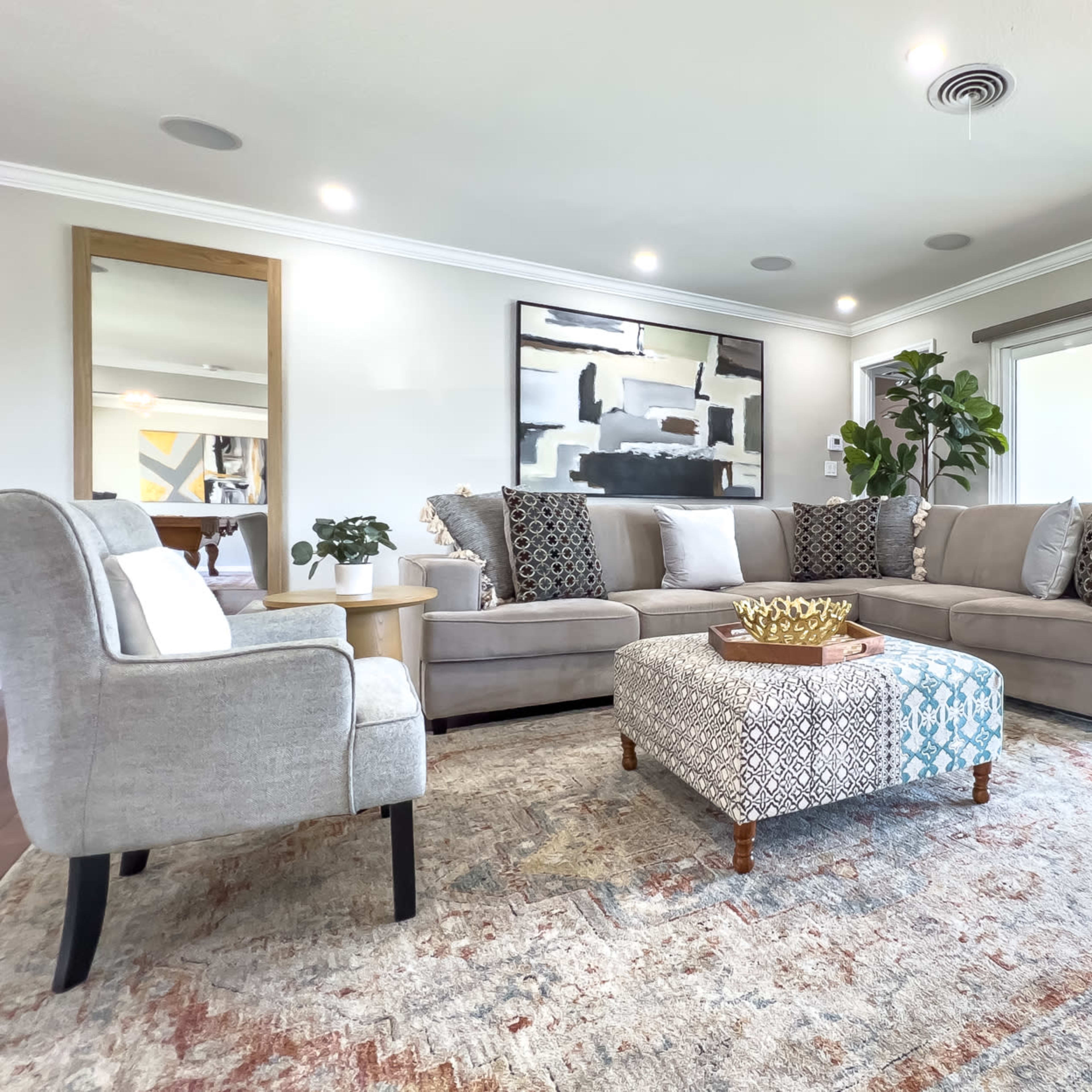 The living room features a sectional sofa, a patterned ottoman, a coffee table, and large sliding glass doors leading to an outdoor patio.