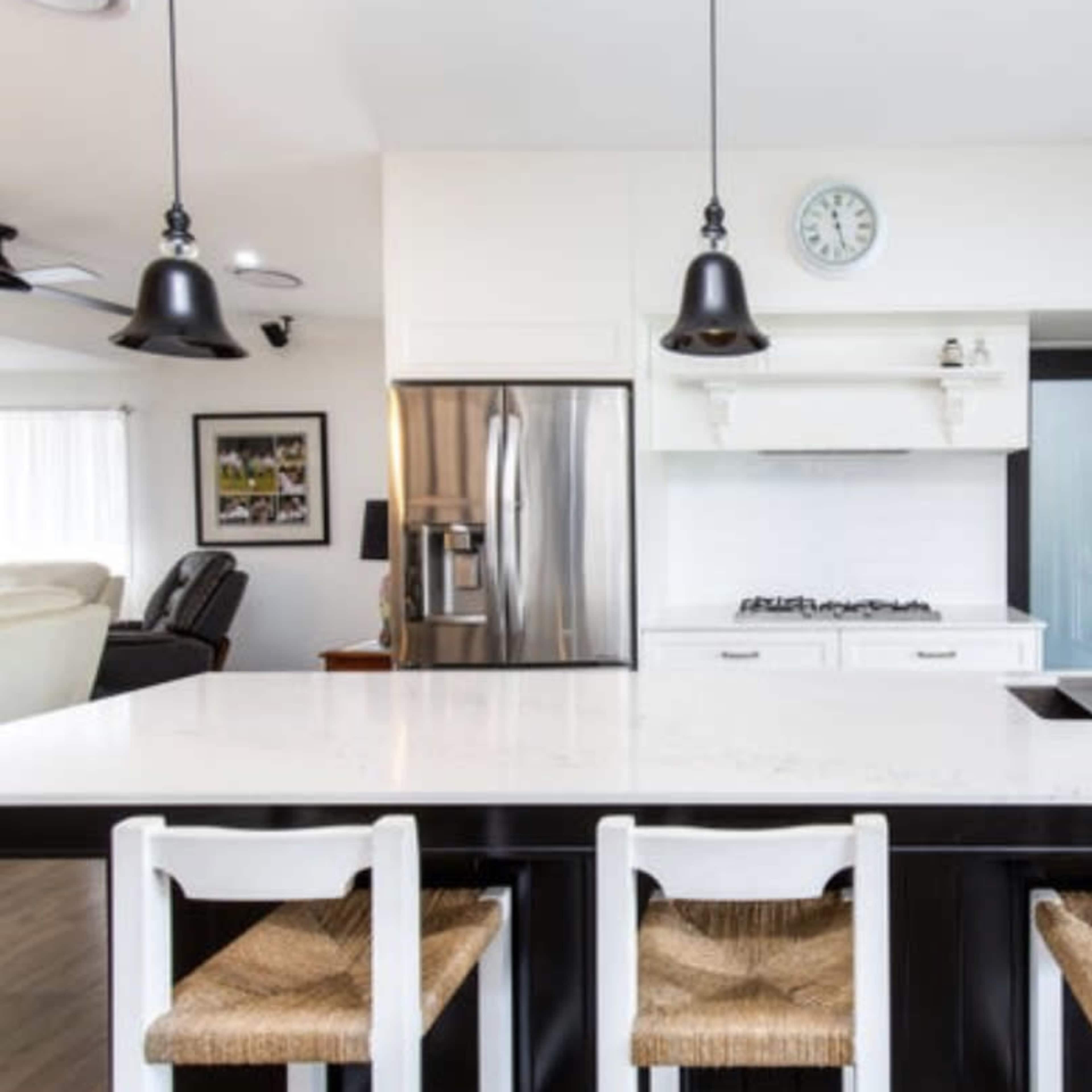 A modern kitchen features a large white island with black seating, stainless steel appliances, and pendant lighting.