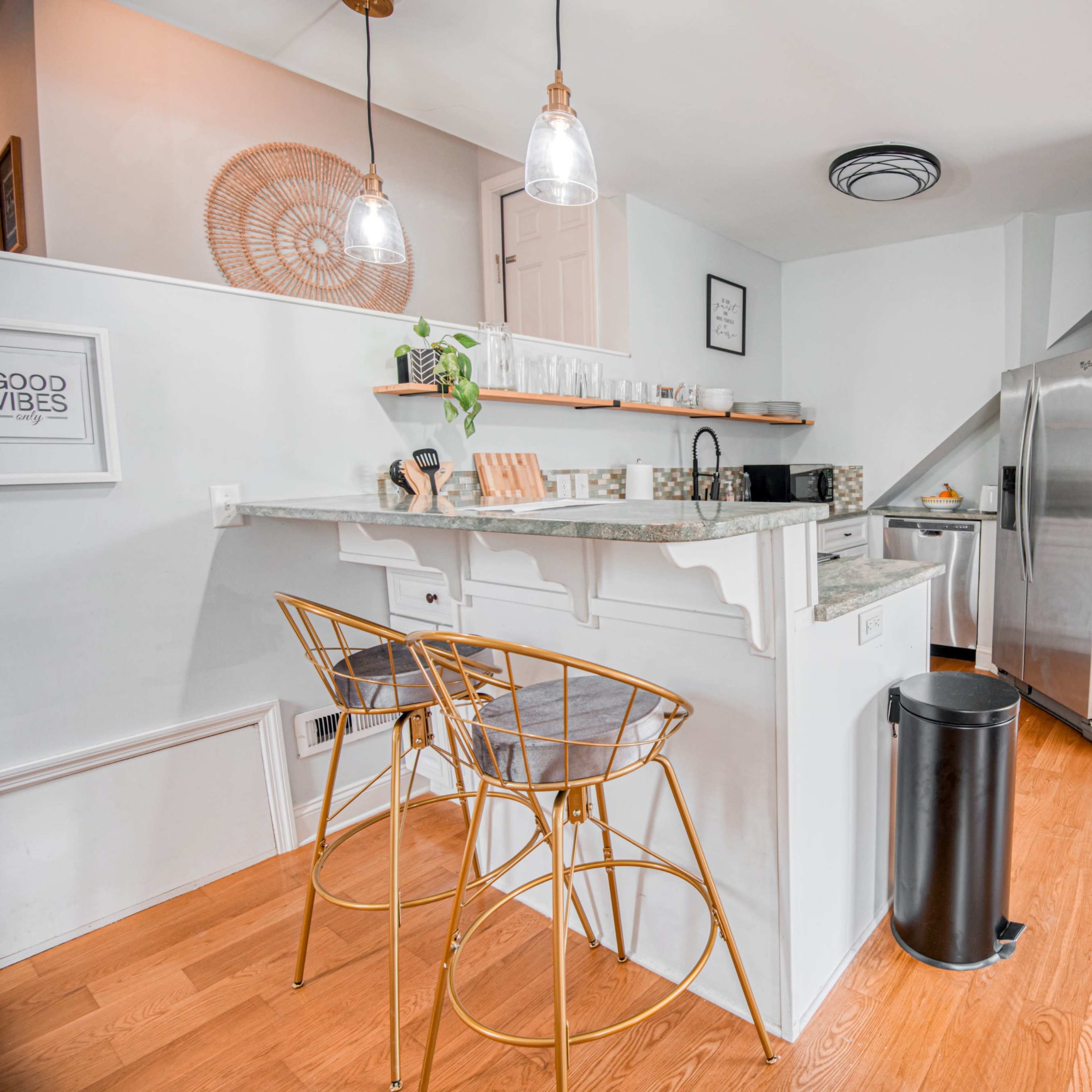 A modern kitchen featuring a bar area with two stools, stainless steel appliances, and light-colored cabinetry.