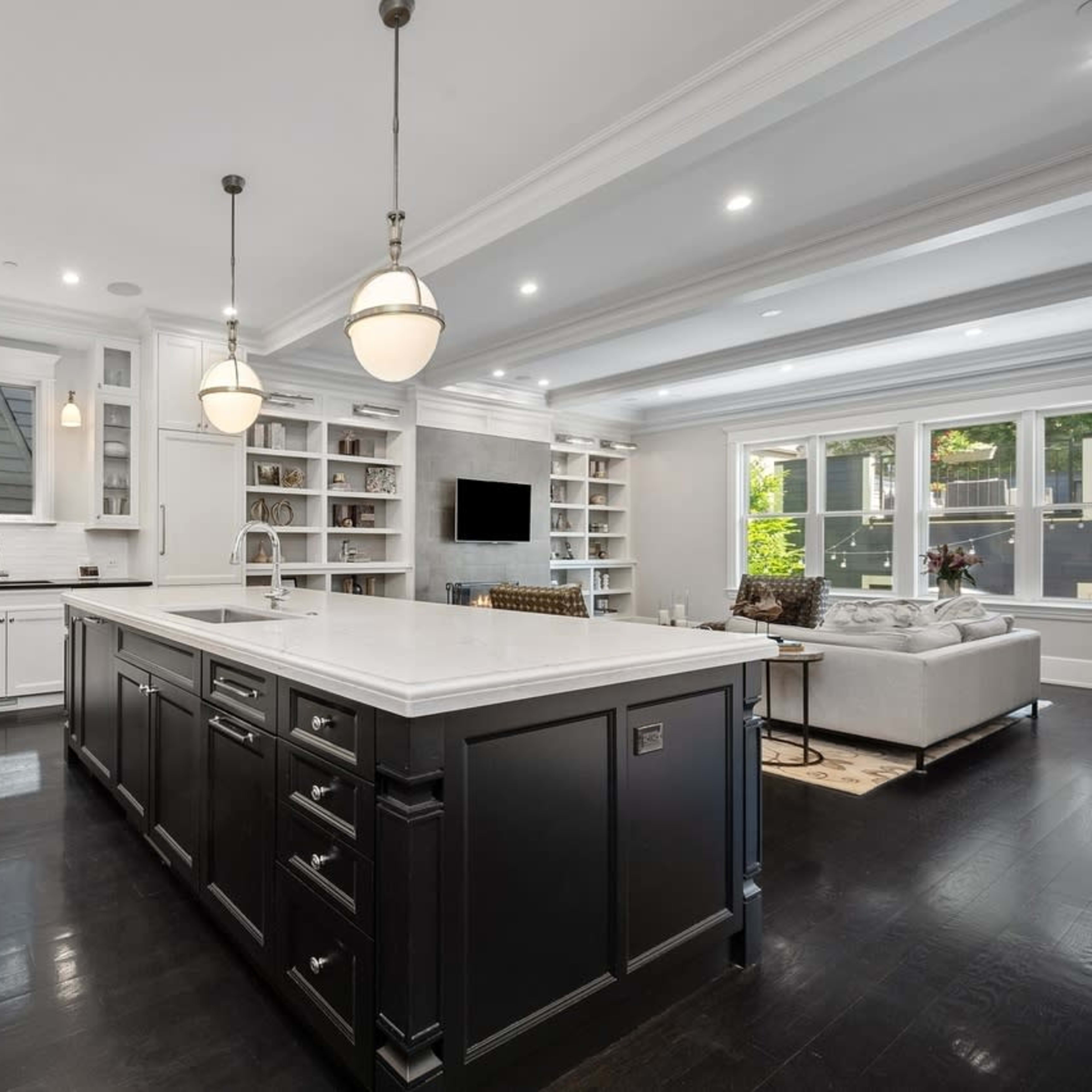 A modern kitchen features an island with a white countertop, dark cabinetry, and stainless steel appliances, illuminated by pendant lights.