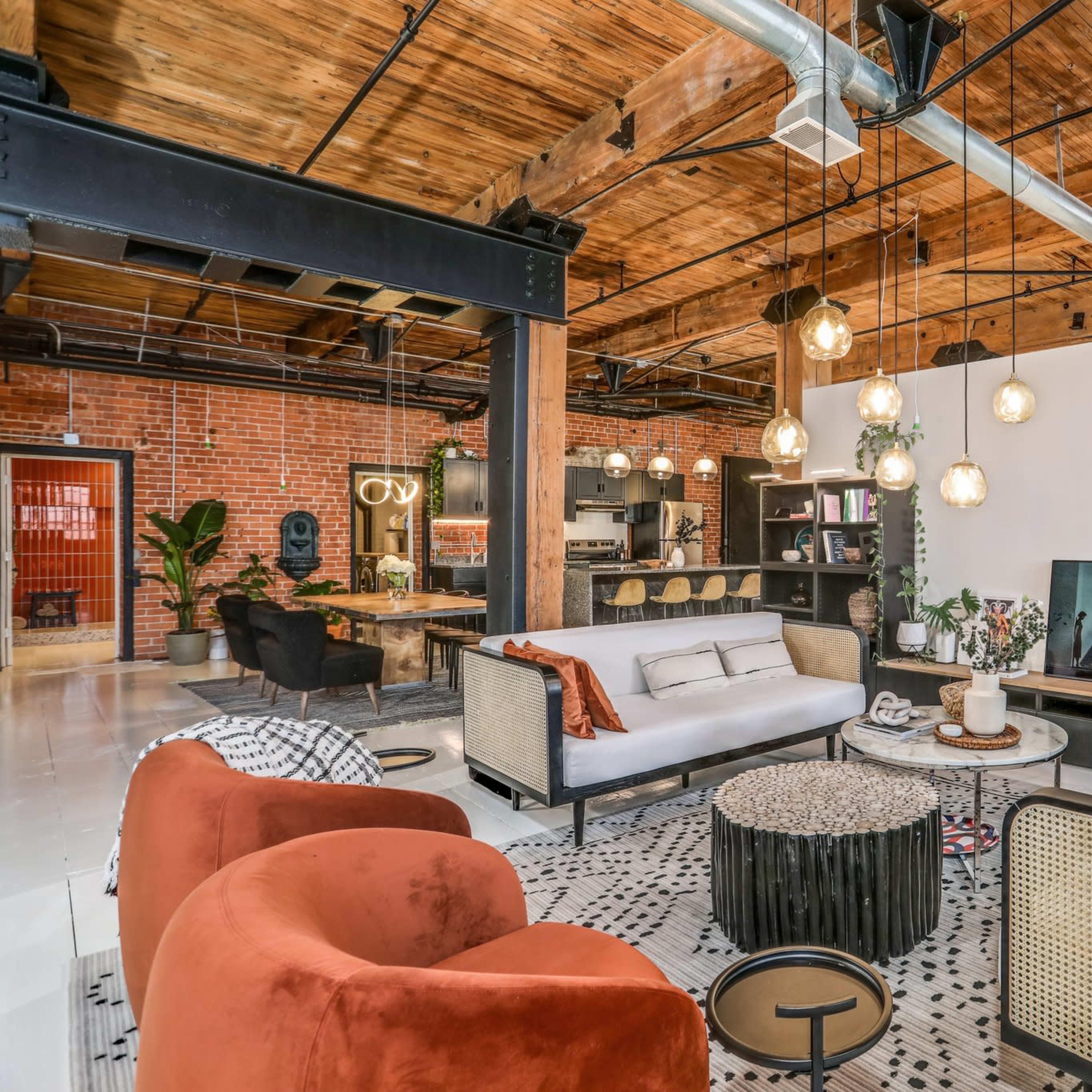 A spacious living area with exposed wooden beams, a mix of modern and vintage furniture, and decorative plants.