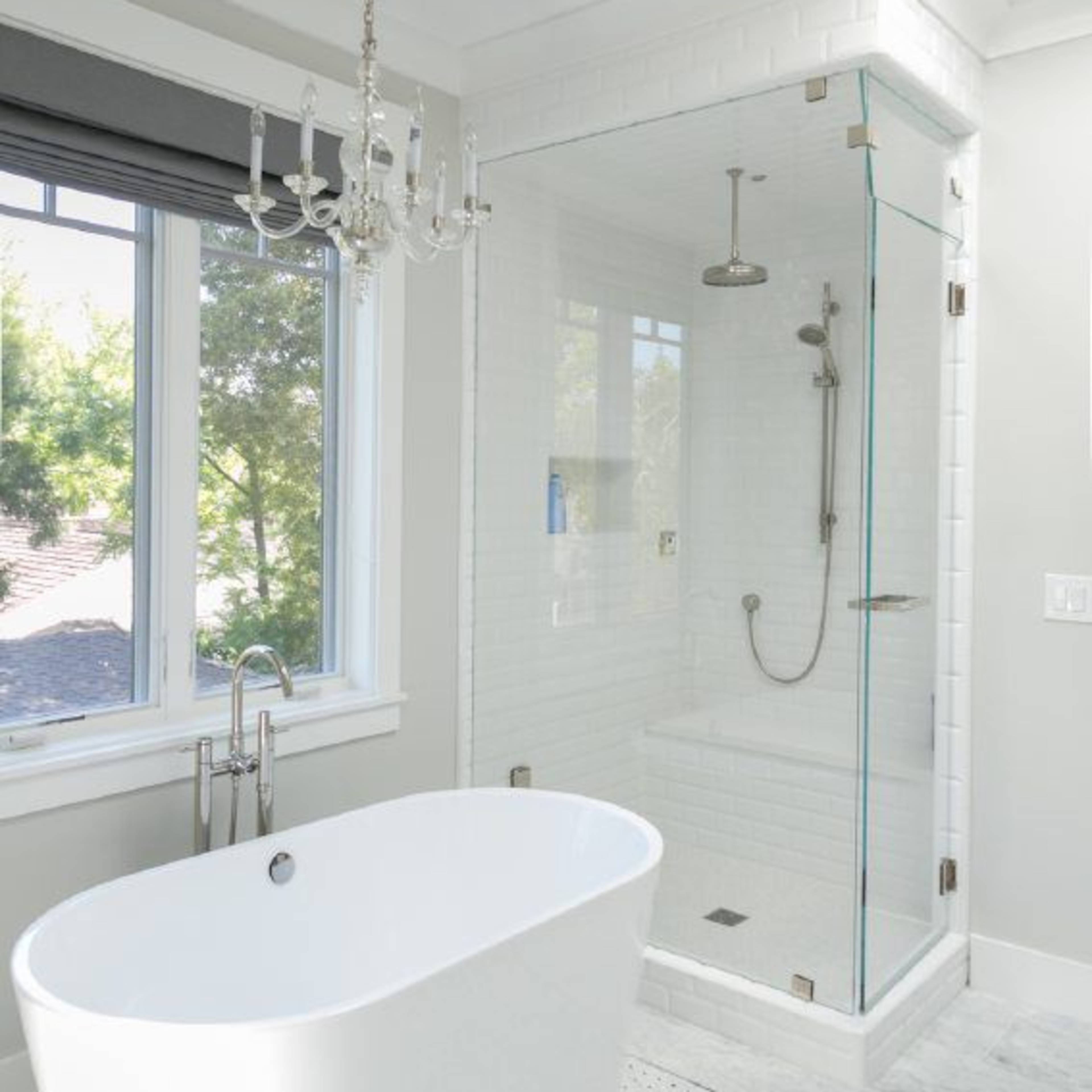 A modern bathroom featuring a freestanding white bathtub, a glass-enclosed shower, and large windows allowing natural light to enter.