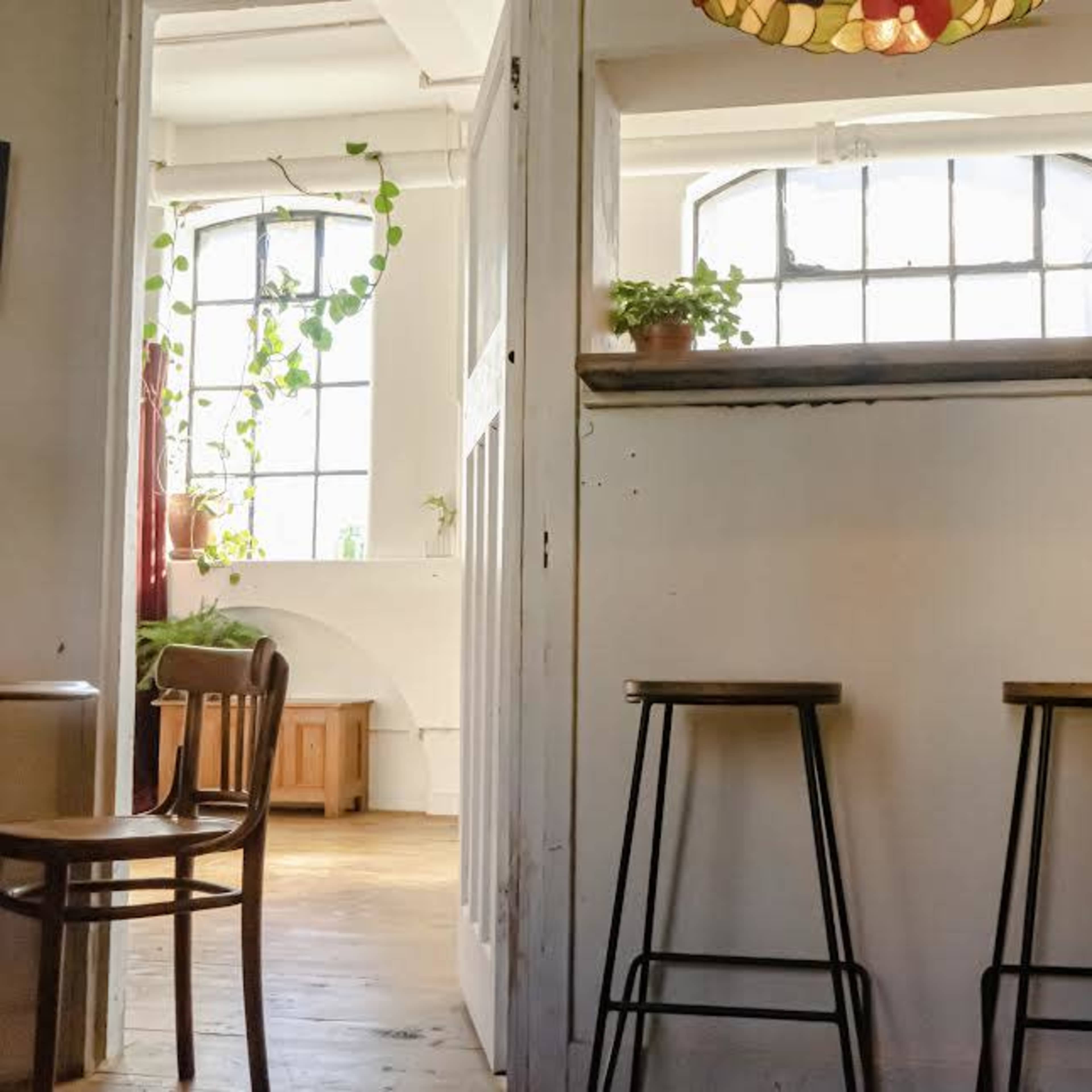 A room with a doorway leading to another area, featuring two metal stools and a window with a plant on the sill.