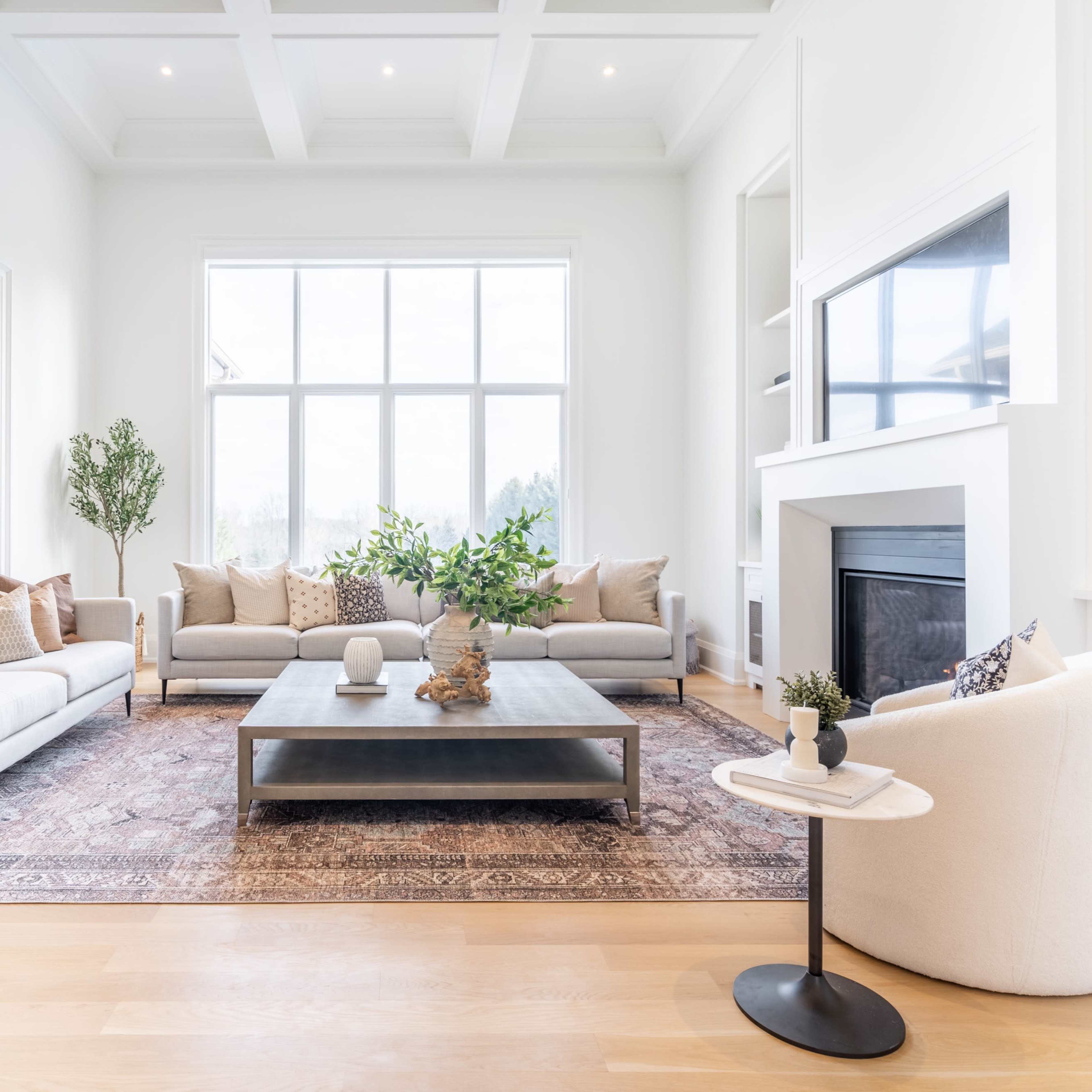 A modern living room features light-colored sofas, a central coffee table, and a large window illuminating the space.