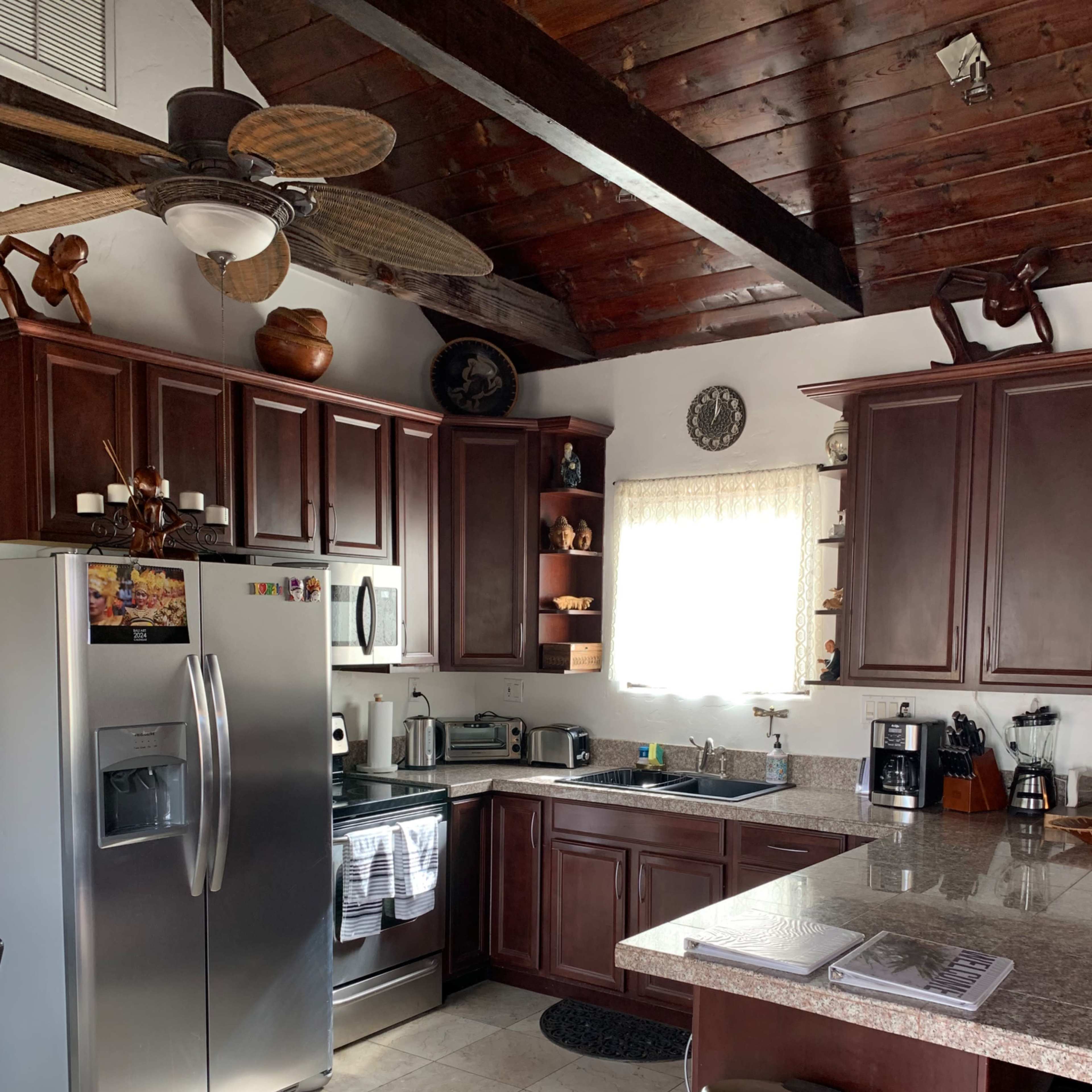 A modern kitchen features dark wooden cabinets, a stainless steel refrigerator, and various appliances set against a tiled floor.