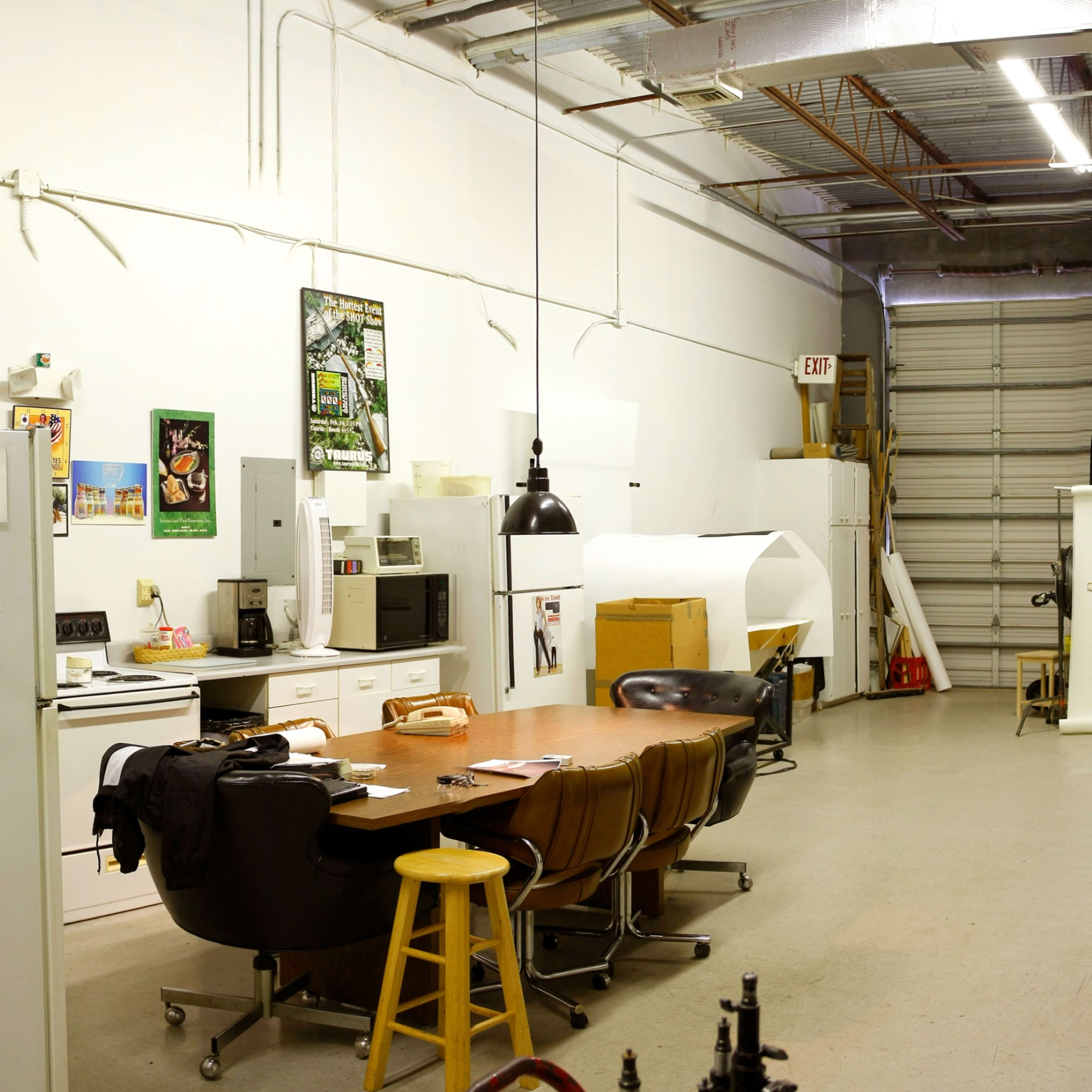 A spacious studio or workshop with various workstations, including tables, chairs, and equipment, along with storage cabinets and a large backdrop setup.