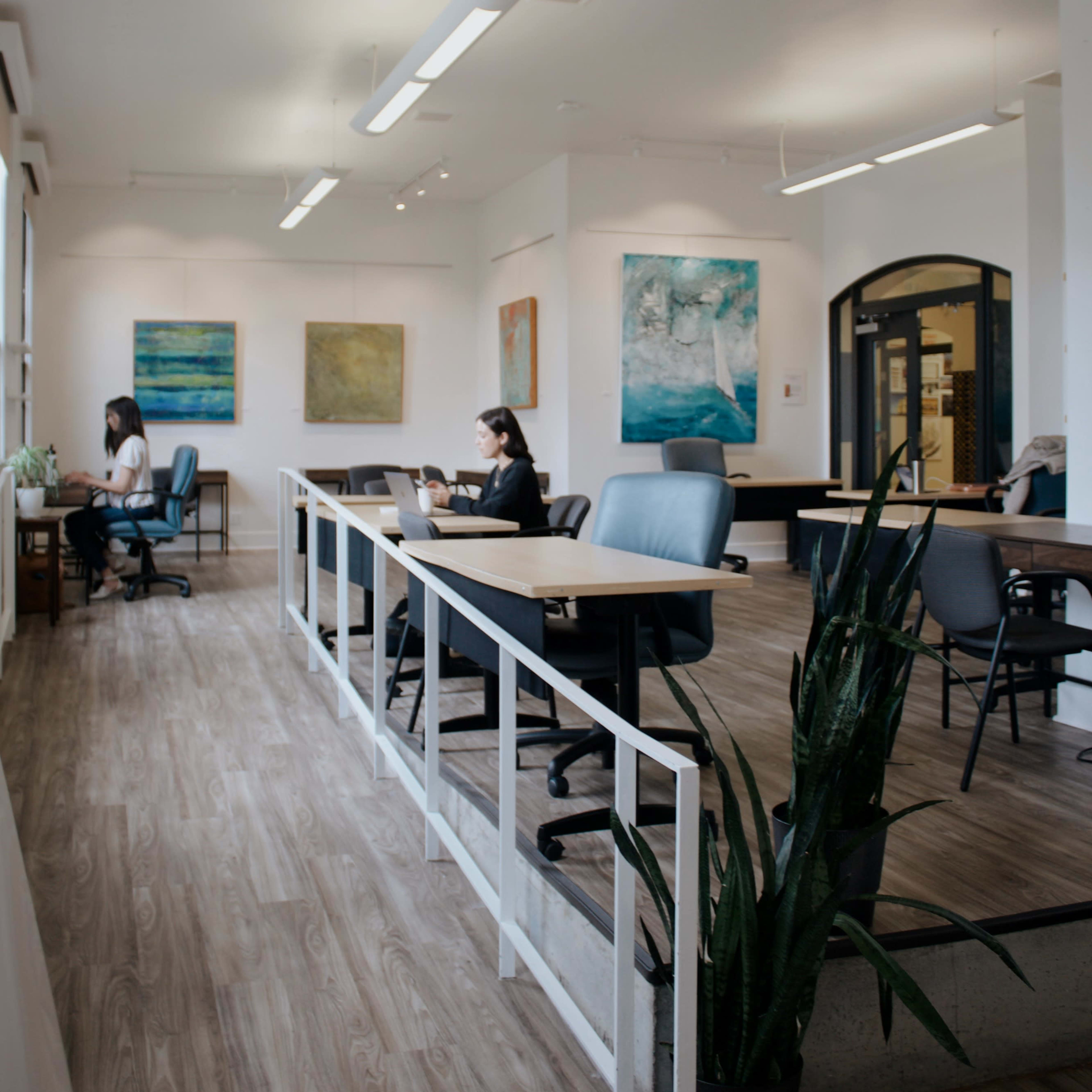 A bright, modern office space with multiple workstations, artwork on the walls, and individuals working at their desks.