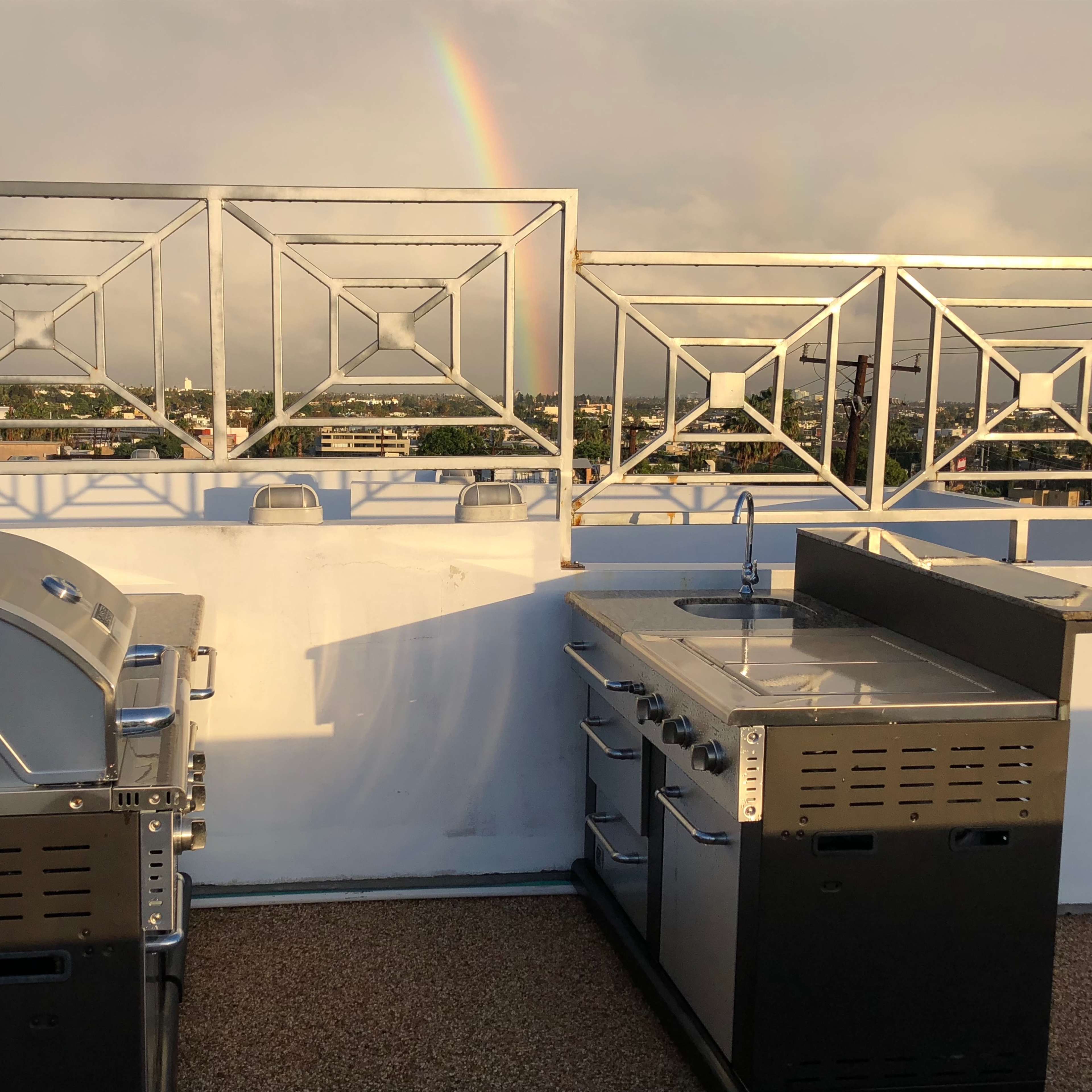 Two stainless steel grills and a cooking station on a rooftop with a rainbow in the background.