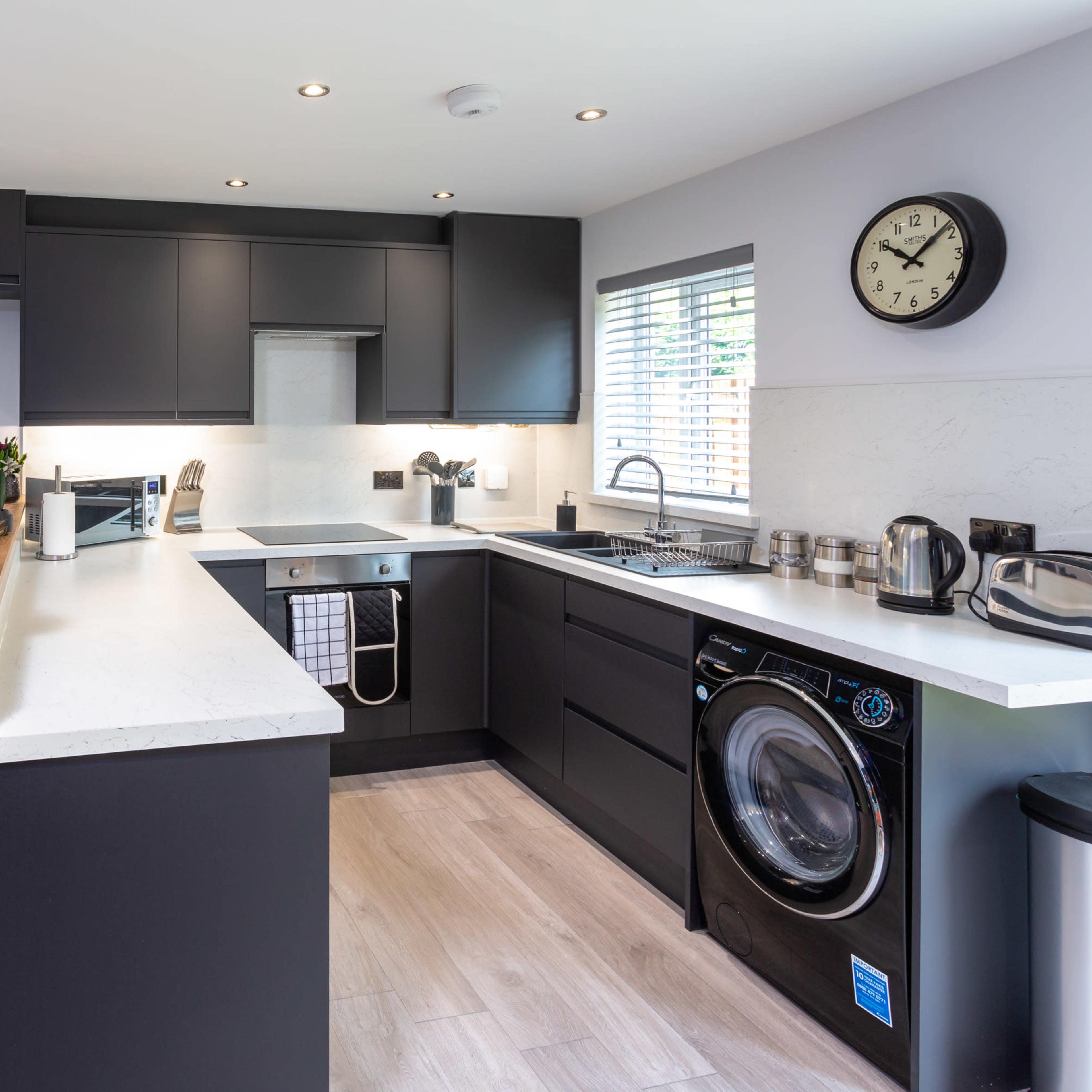 A modern kitchen features dark cabinetry, a white countertop, stainless steel appliances, and a laundry machine integrated into the design.