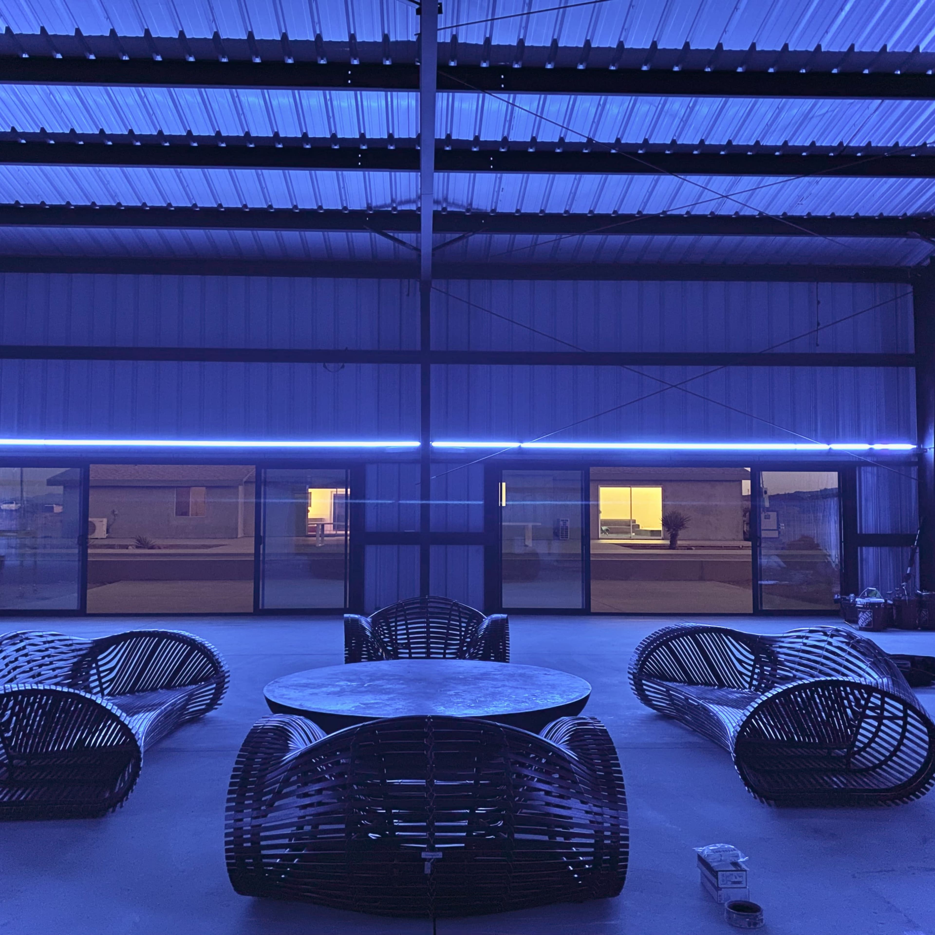 A spacious indoor area with modern woven furniture arranged around a circular table, illuminated by blue lights along the ceiling.