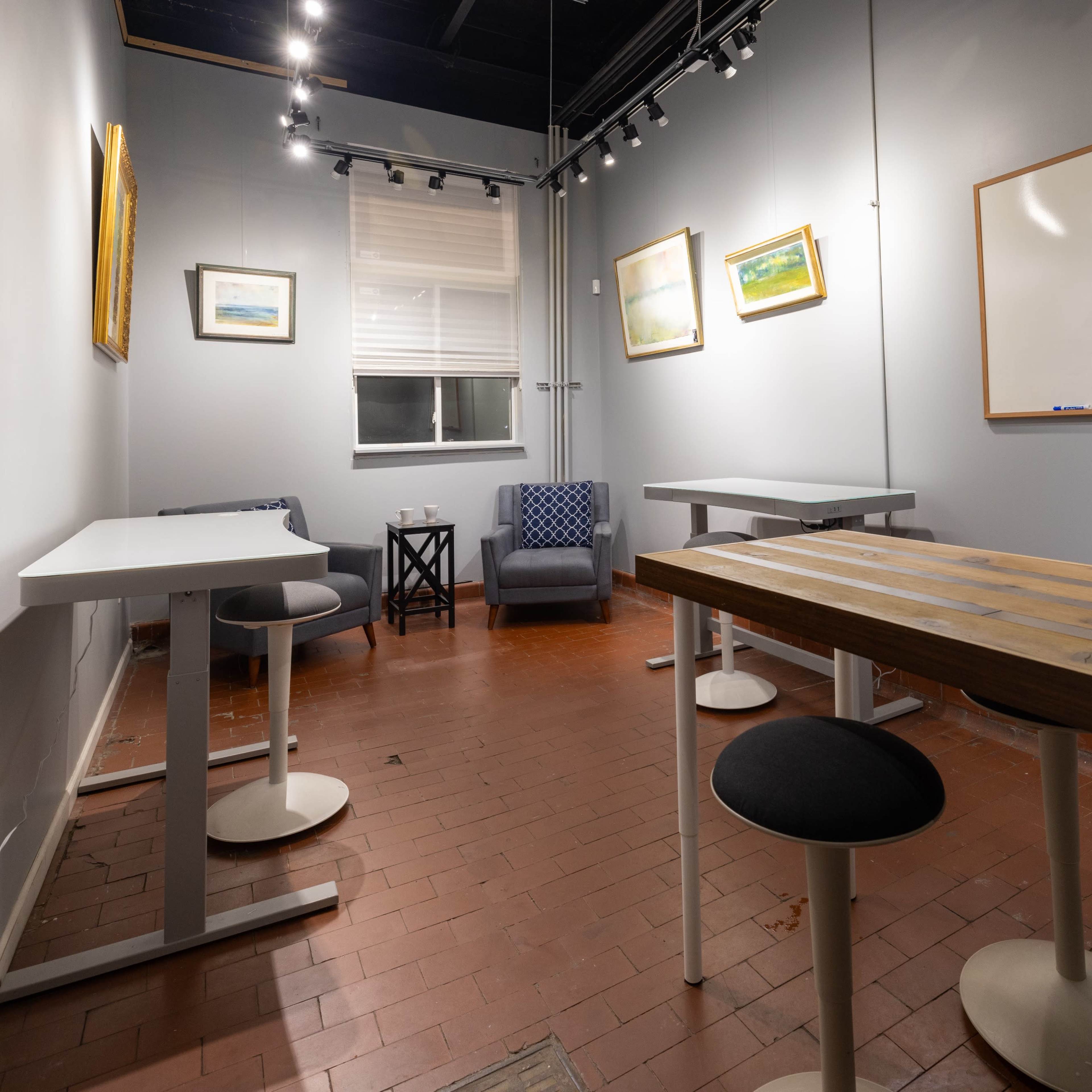 A small, minimally furnished meeting room with two tables, a chair, and wall-mounted artwork.