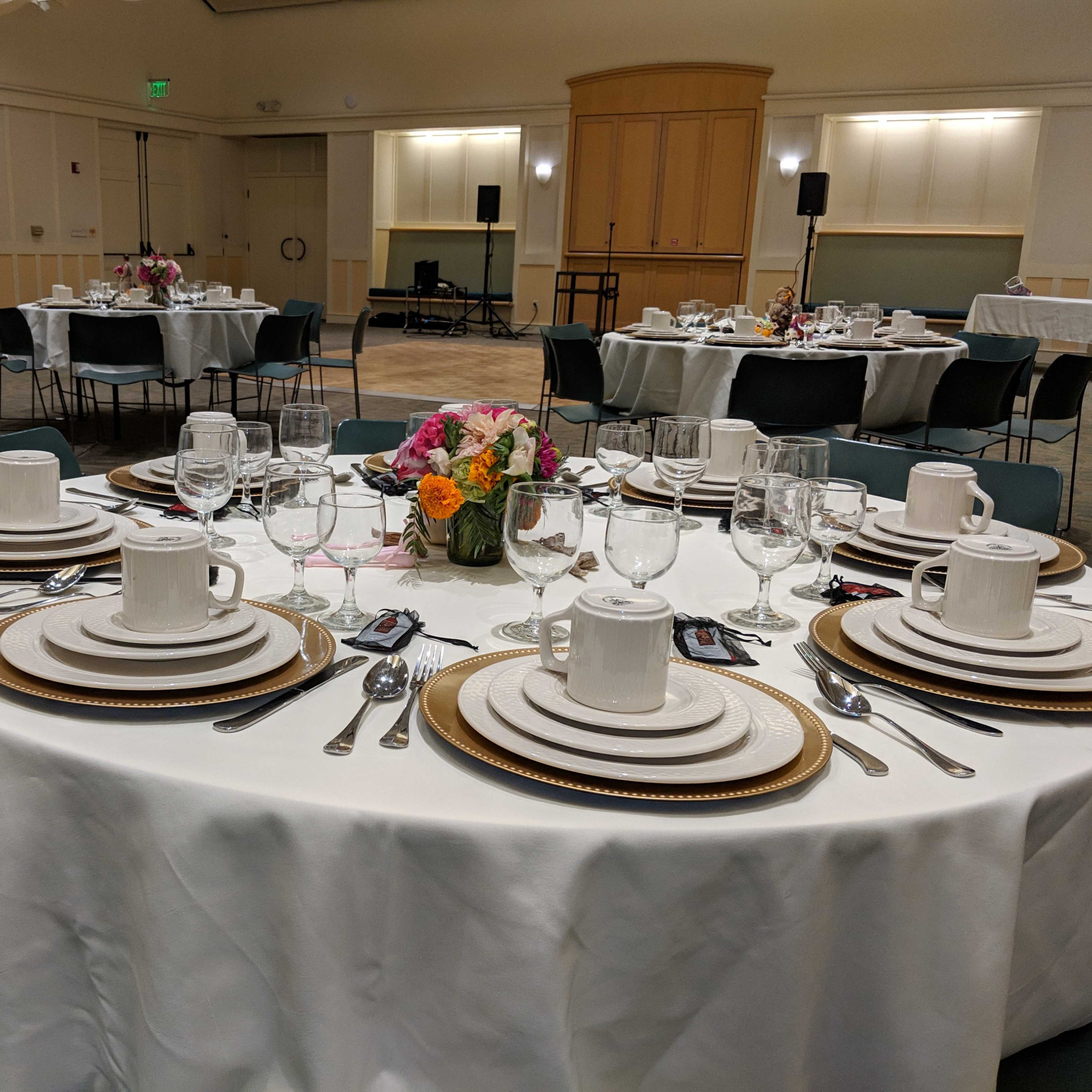 A banquet hall set up with round tables elegantly arranged with white tablecloths, place settings, wine glasses, and floral centerpieces.