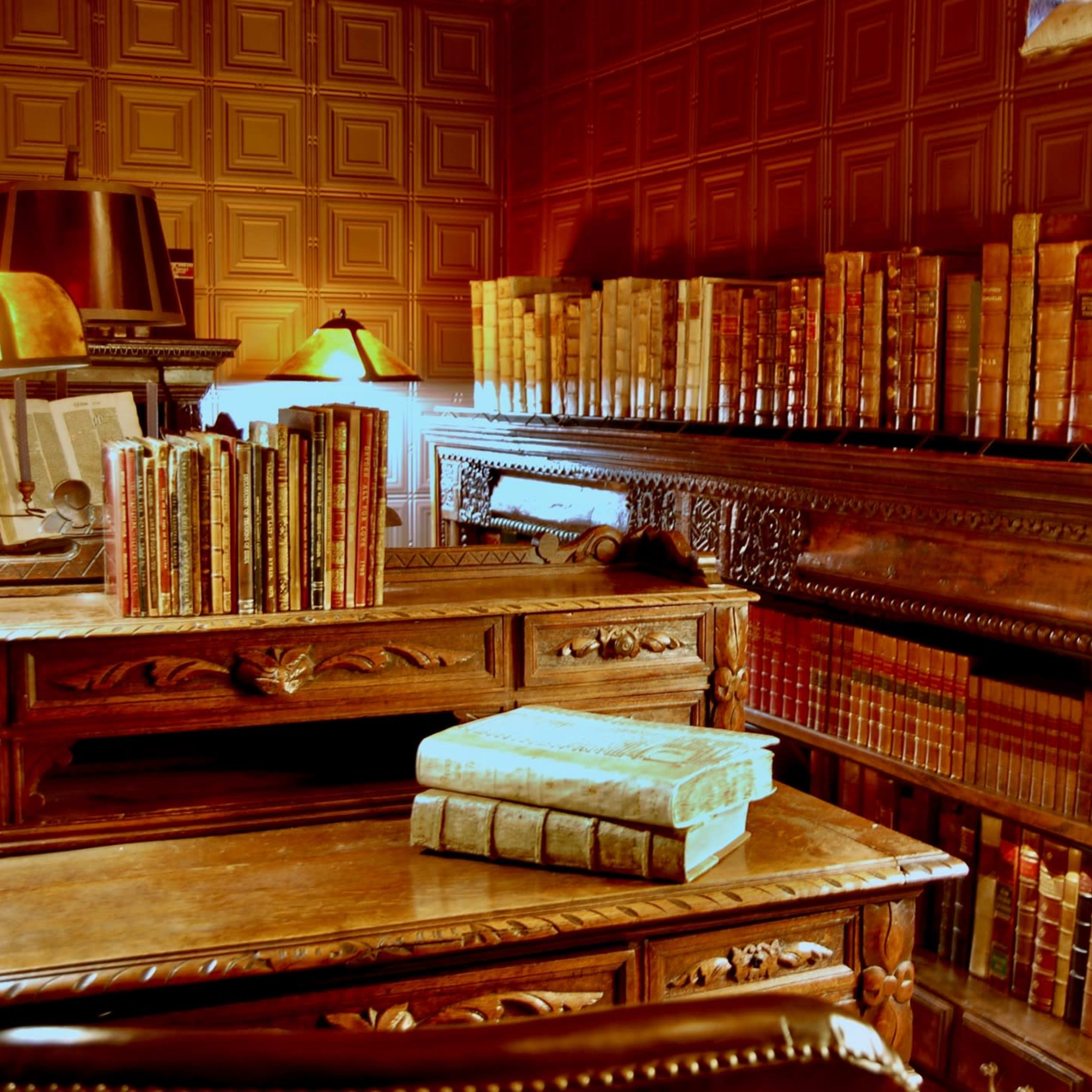 An antique wooden desk surrounded by shelves filled with books in a warmly lit library.
