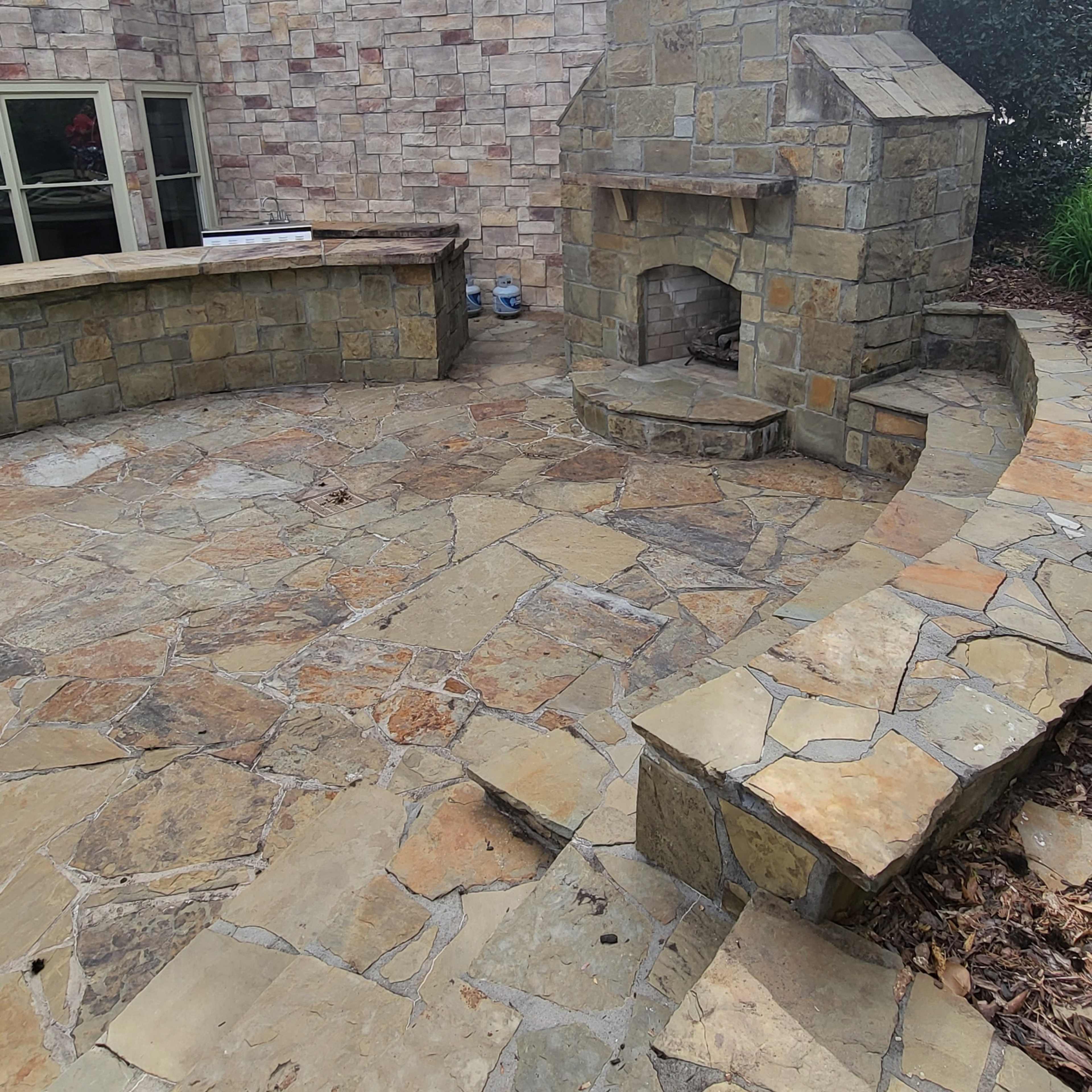 A stone patio with a built-in outdoor fireplace and a seating area.