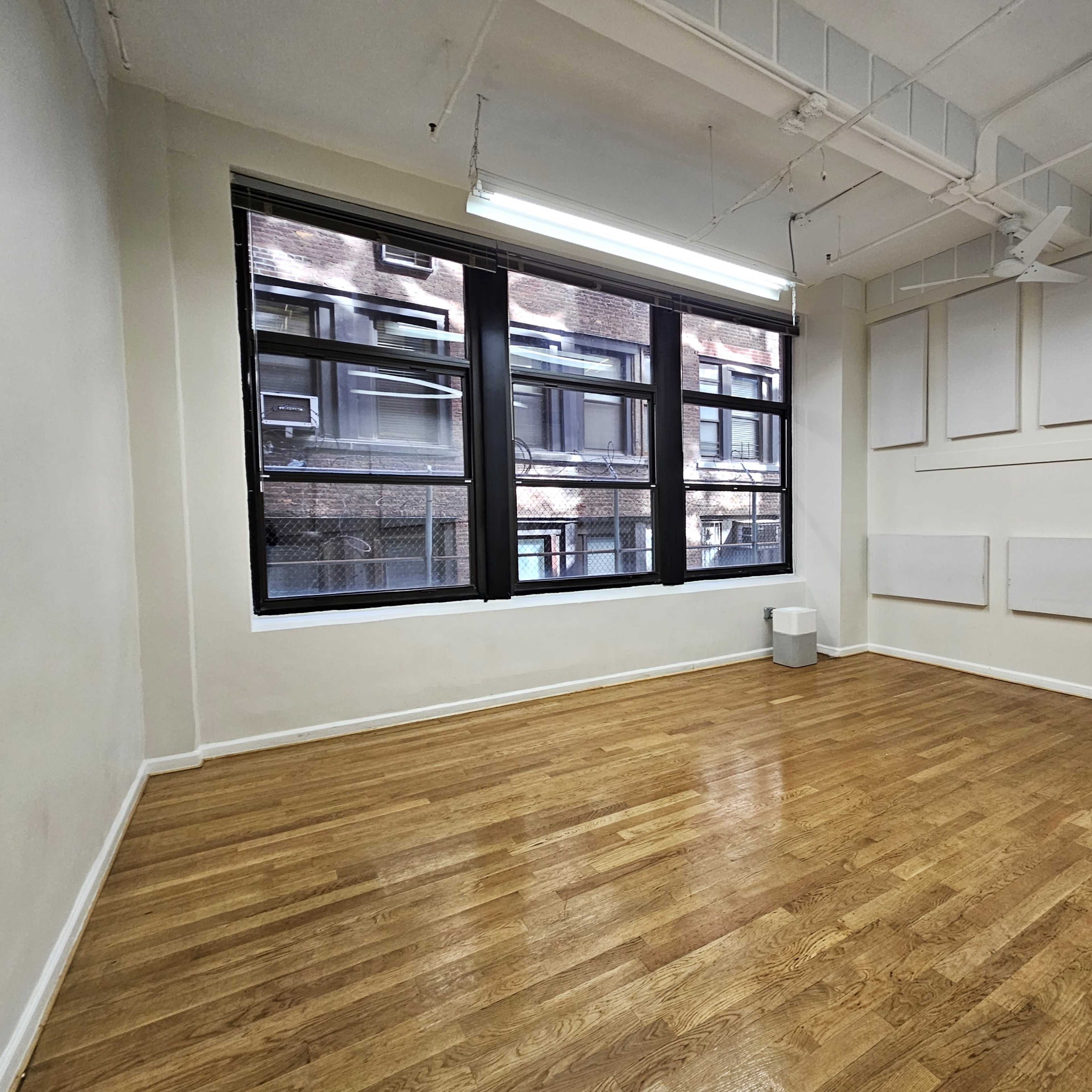 A vacant room with wooden flooring, large windows, and bare walls.