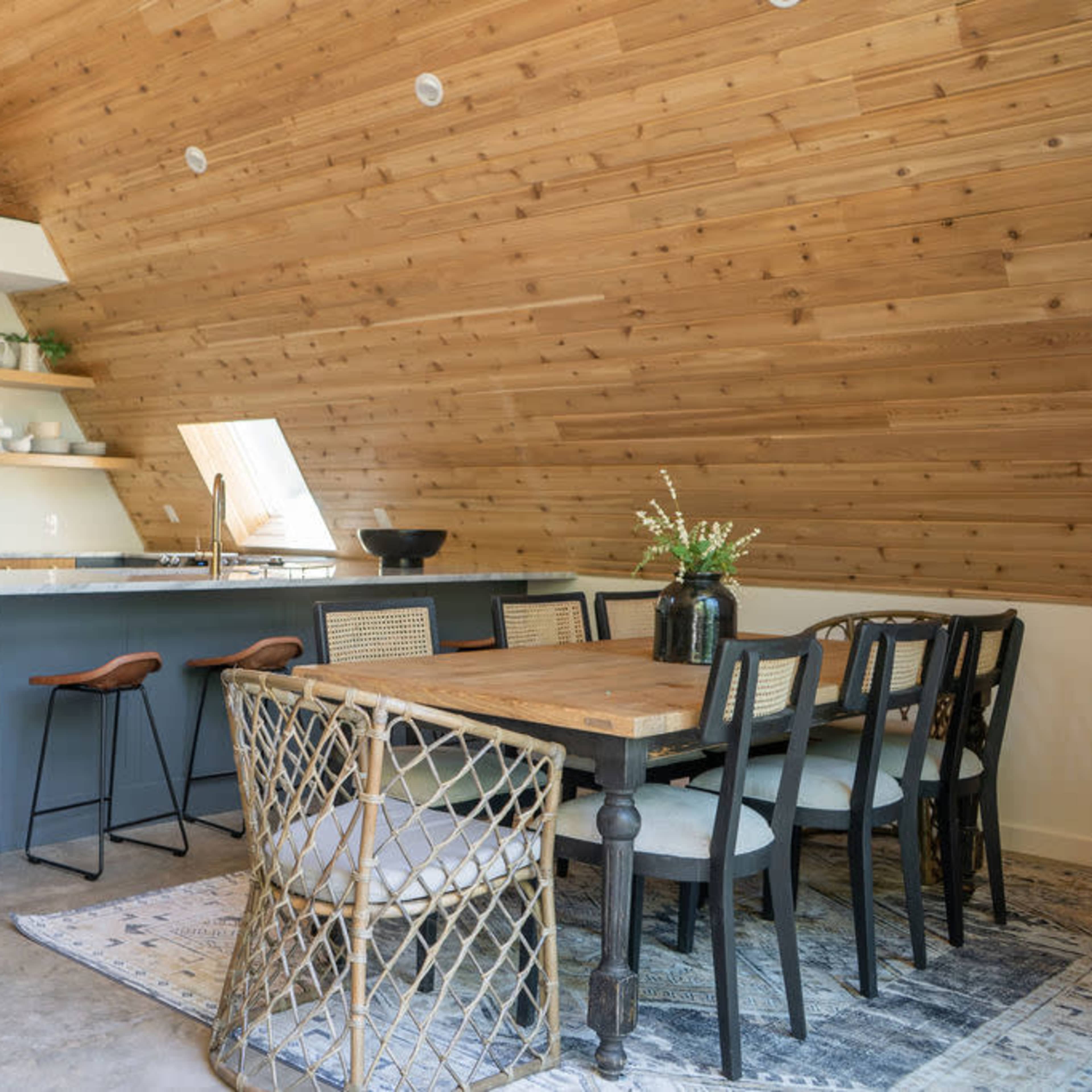 A modern open-concept kitchen and dining area with wooden walls, a large table, and stylish seating arrangements.