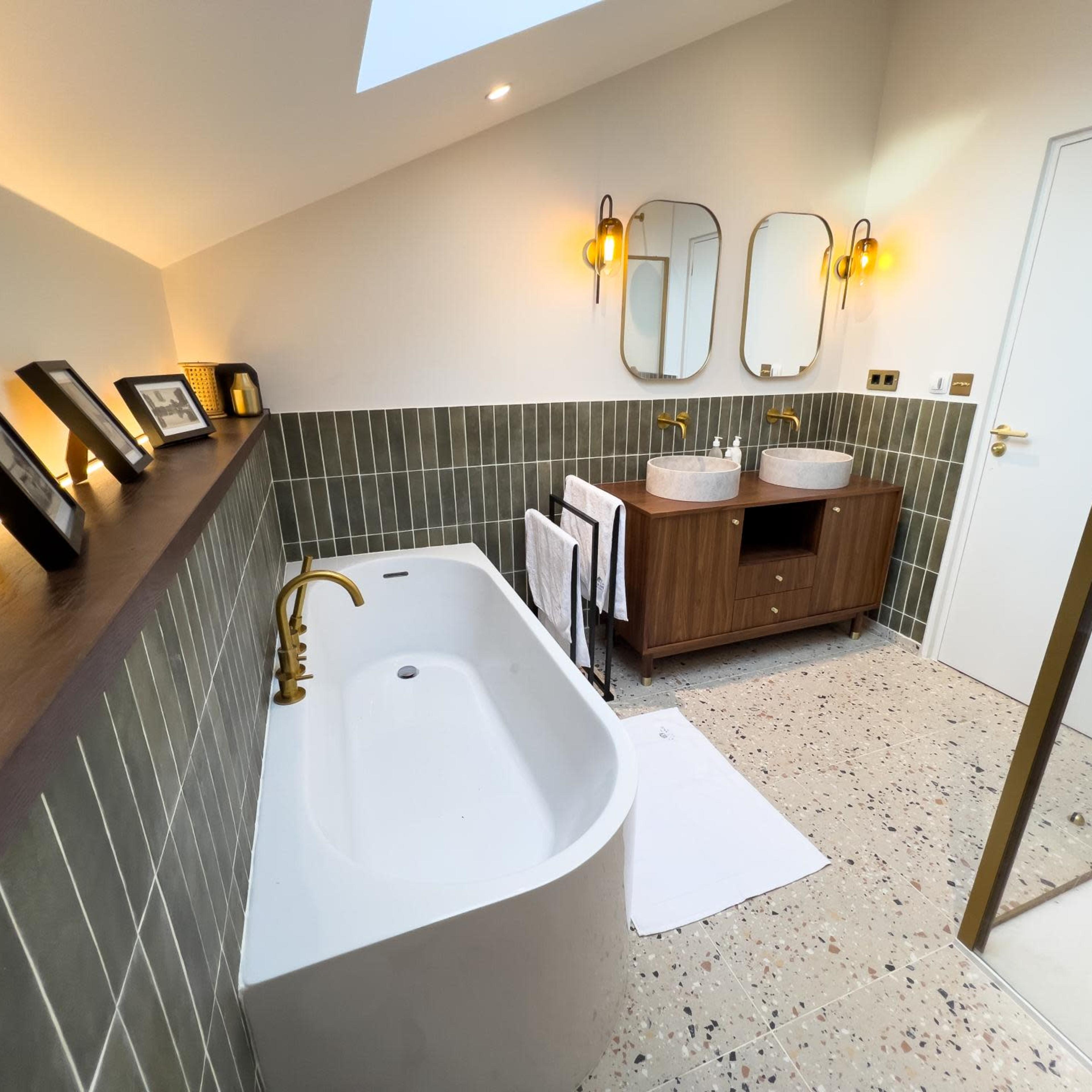 The bathroom features a freestanding tub, a dual sink vanity with round mirrors, and a sliding glass shower door, all set against a backdrop of textured green tiles.