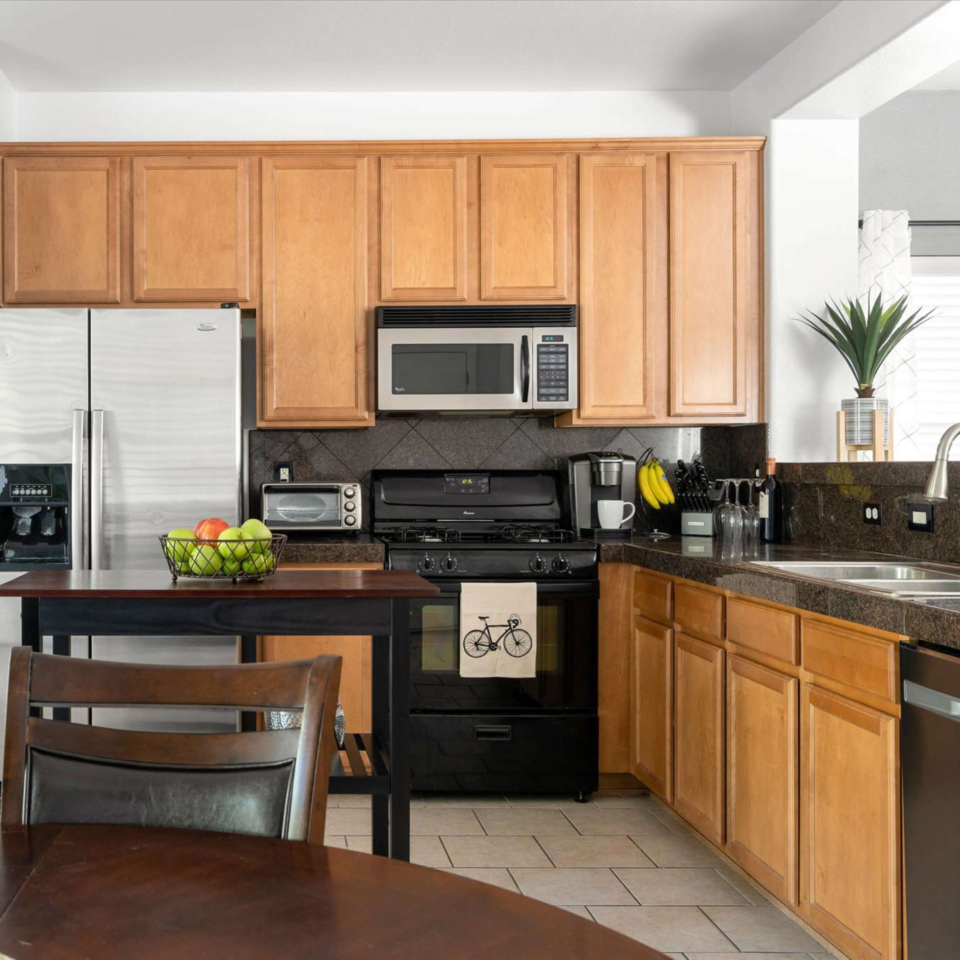 The kitchen features wooden cabinets, stainless steel appliances, and a central island with a fruit bowl, adjacent to a dining table.