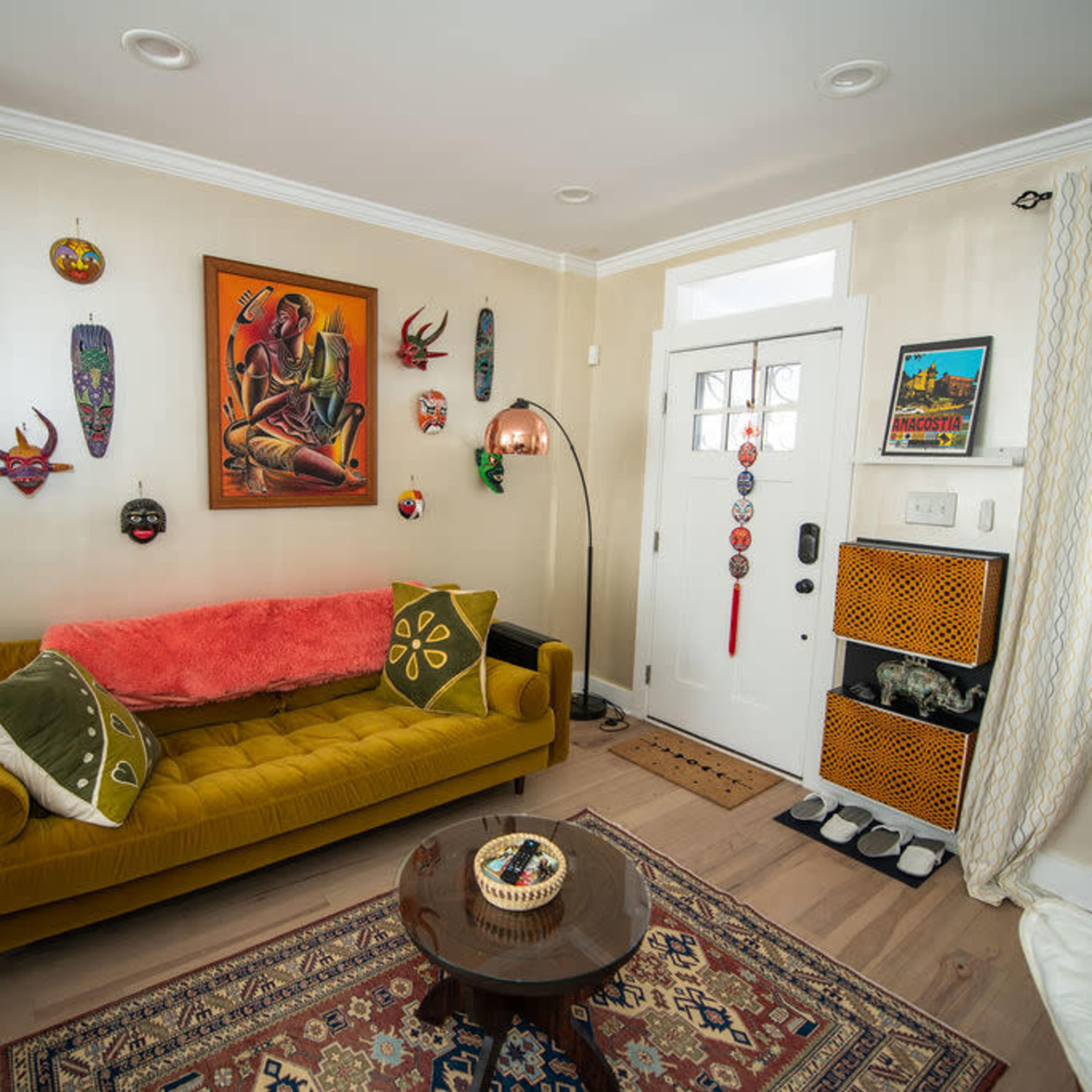 A cozy living room featuring a yellow couch adorned with decorative pillows, a wooden coffee table, and various masks and artwork displayed on the walls.