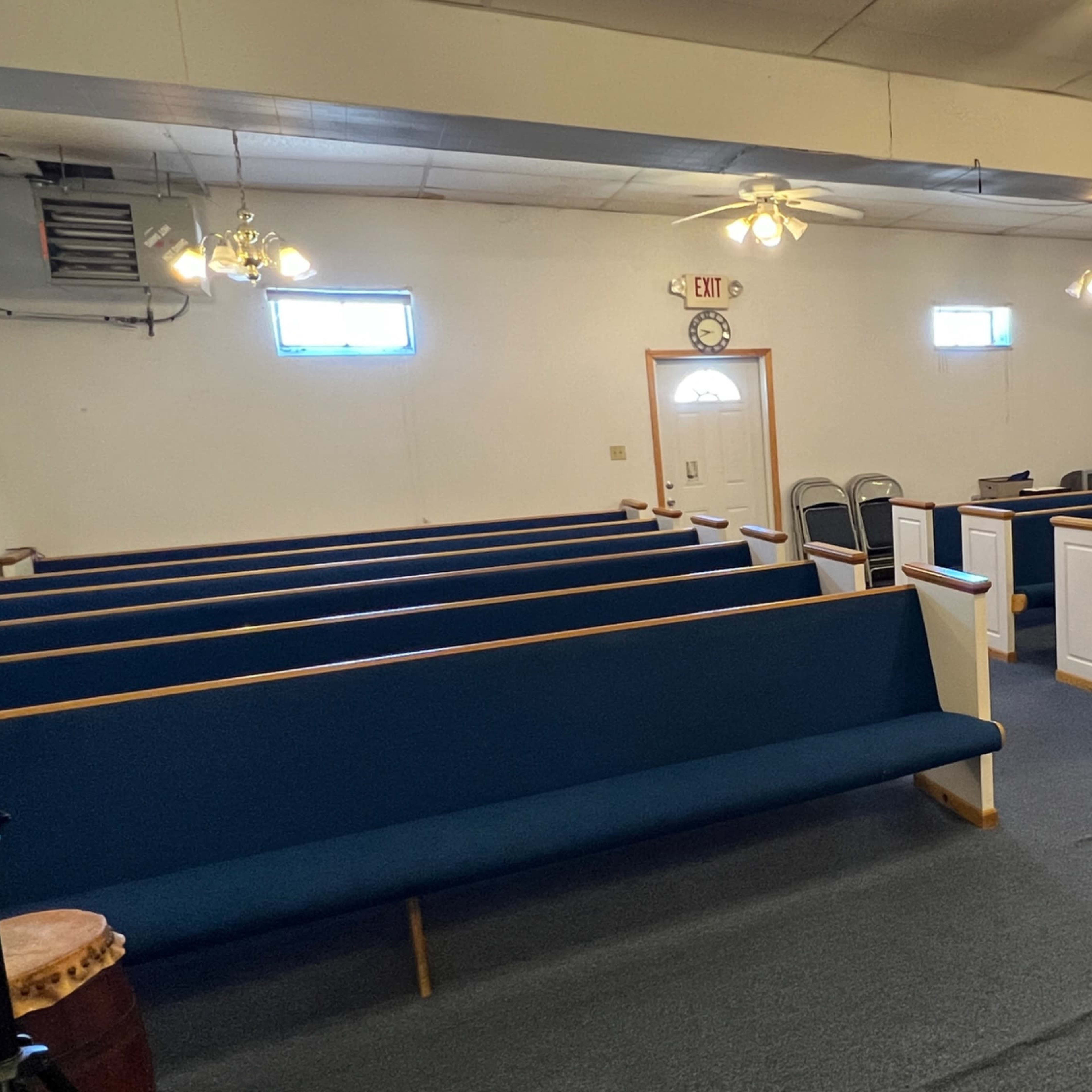 An interior view of a small church or chapel with rows of blue pews, a piano, and a simple altar area.