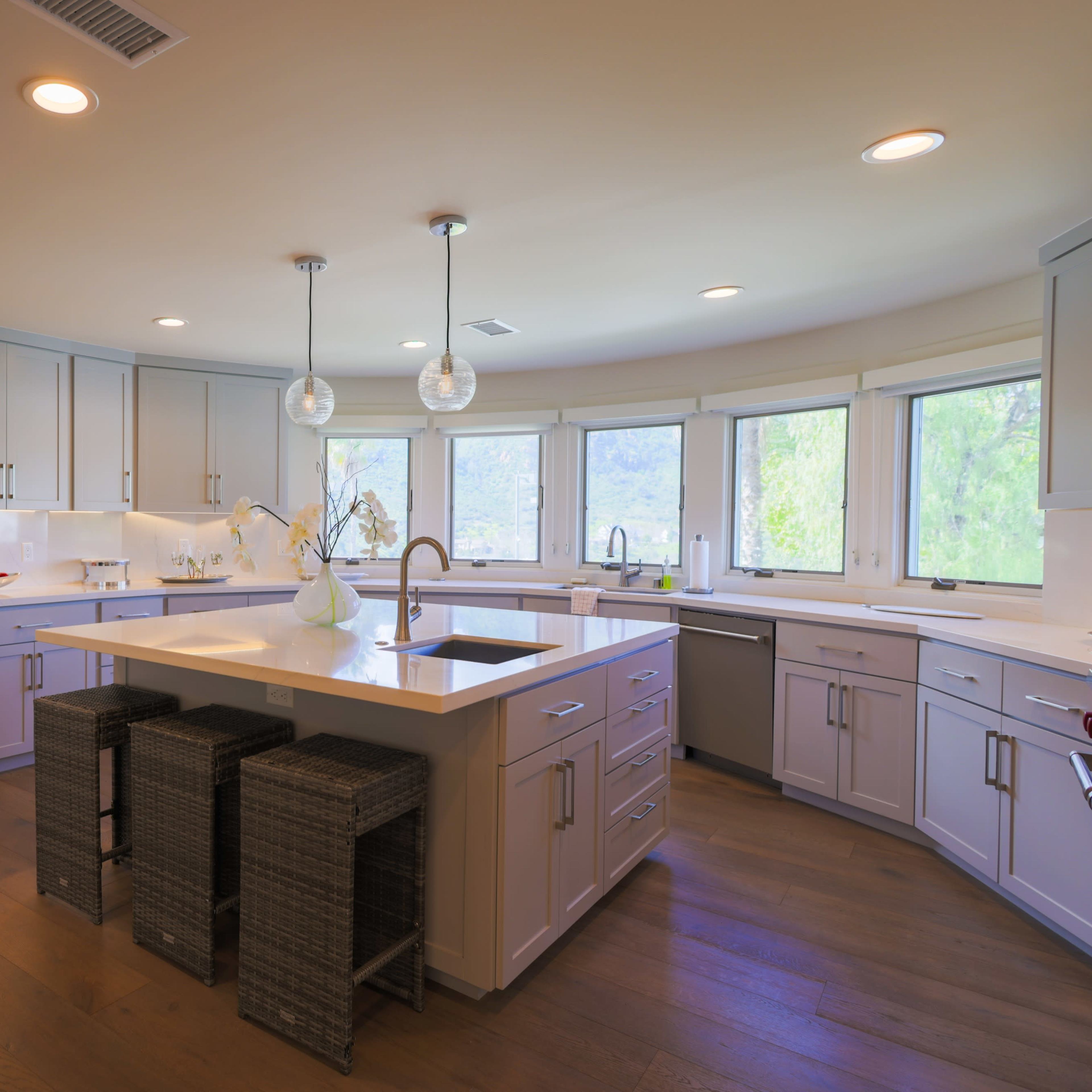 A modern kitchen with gray cabinets, a large island with bar stools, and multiple windows allowing natural light.