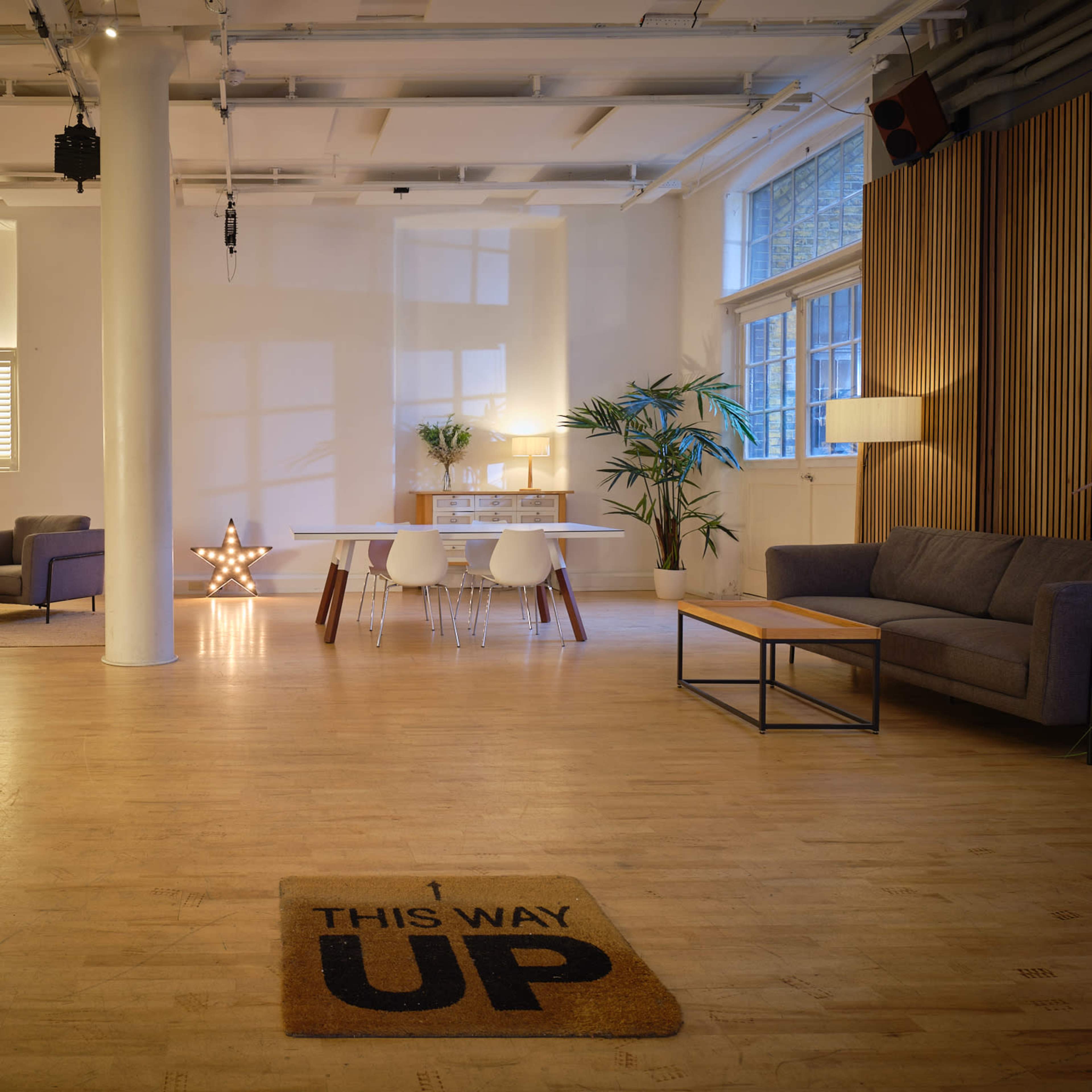 A spacious, well-lit interior with a dining area, seating arrangement, and decorative elements, including a star-shaped light and a welcome mat that reads "THIS WAY UP."