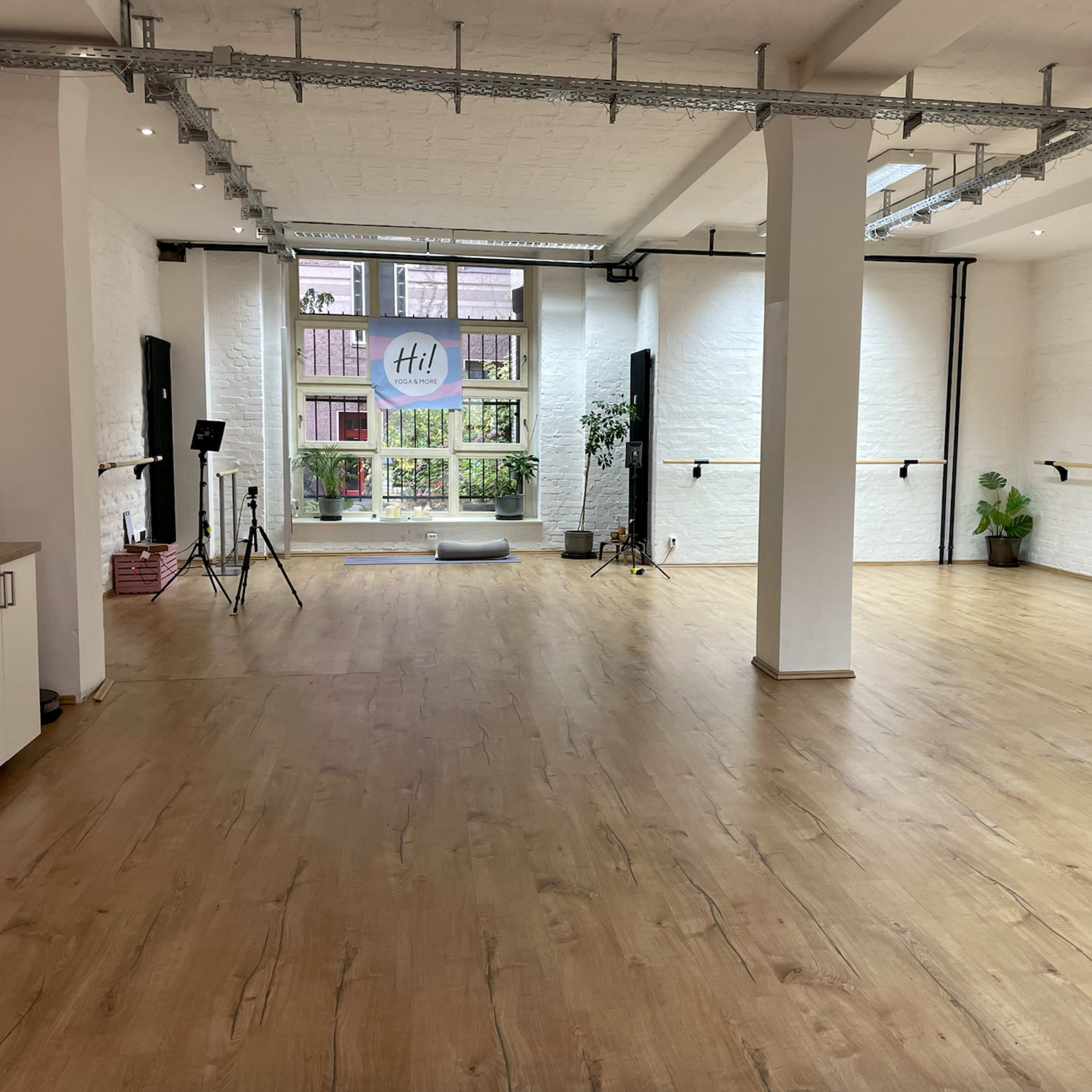A spacious, well-lit dance studio featuring wooden flooring and large windows with a view of greenery outside.