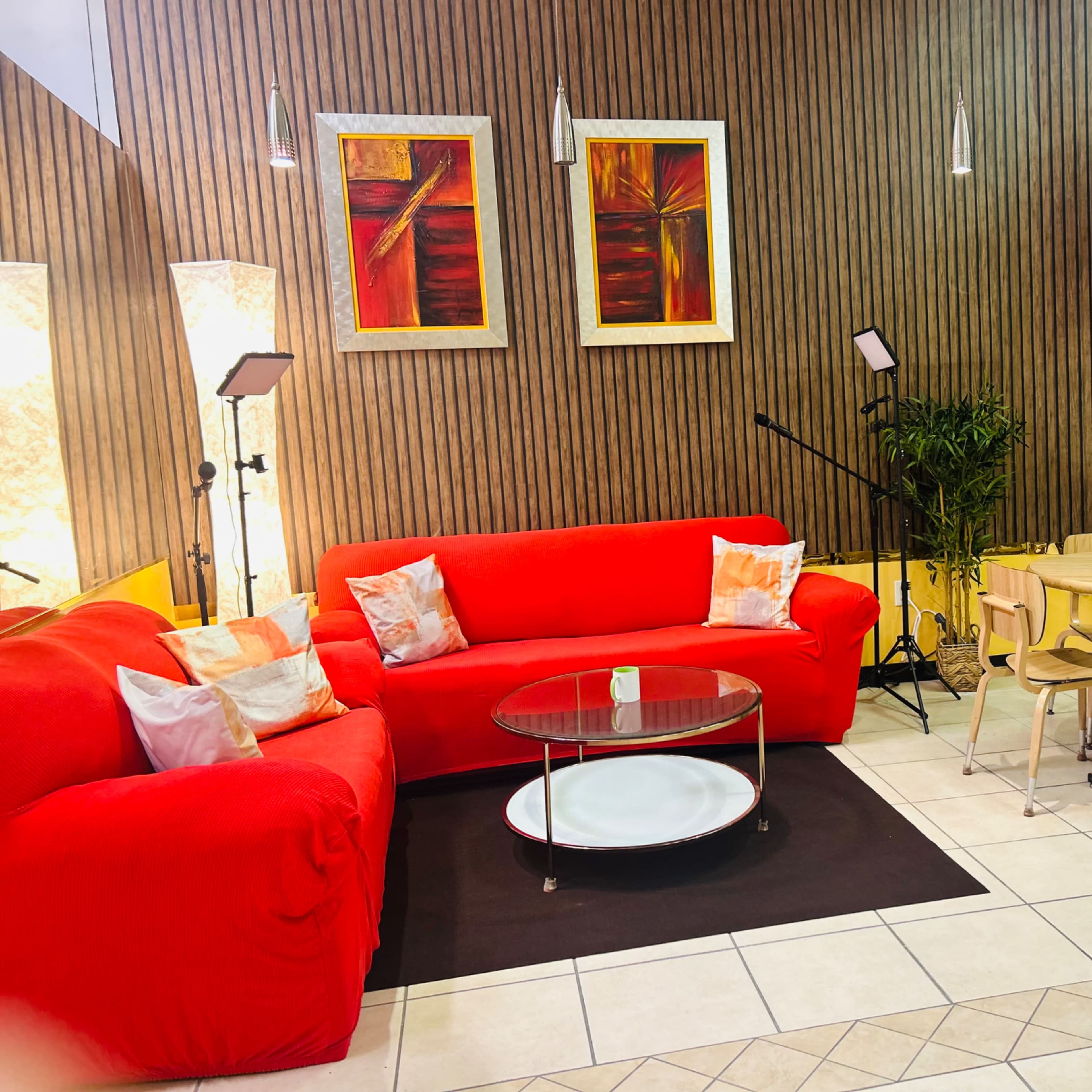 A brightly colored living room features a red couch, a circular coffee table, wooden dining chairs, and wall-mounted artwork.