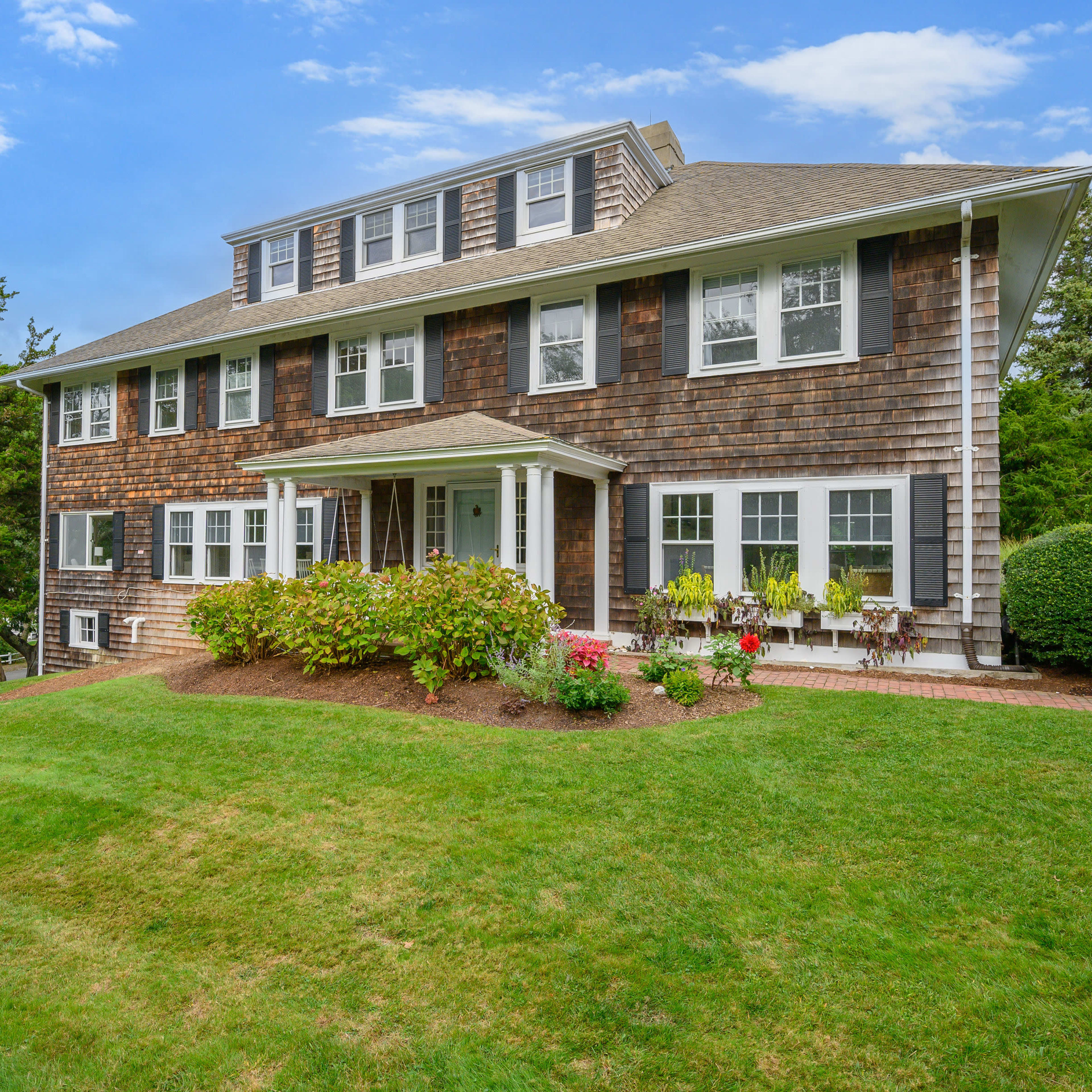 A large, two-story house with a wooden exterior, surrounded by a well-maintained lawn and shrubs.