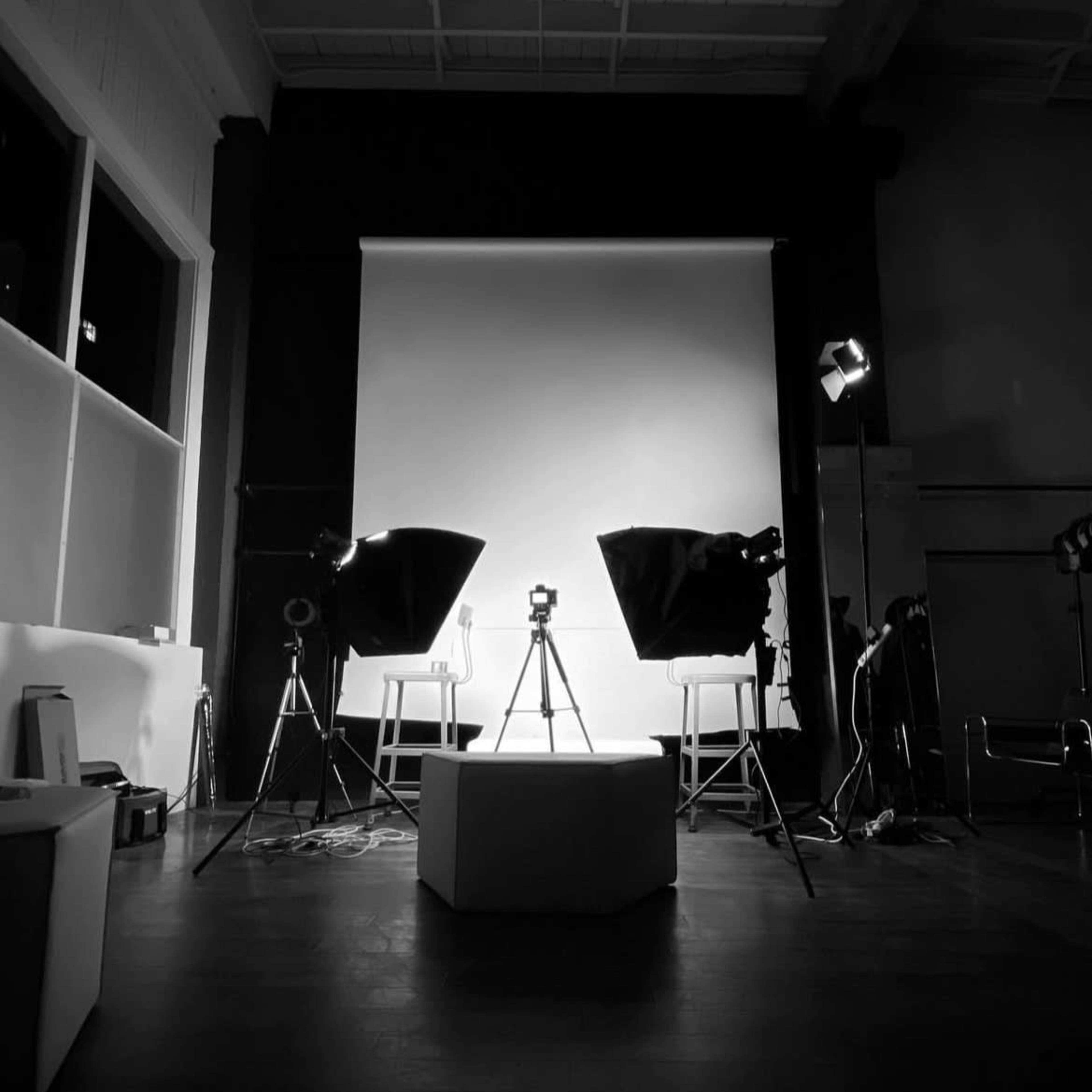 A studio setup with two tripods facing a white backdrop, accompanied by lighting equipment and a central pedestal.