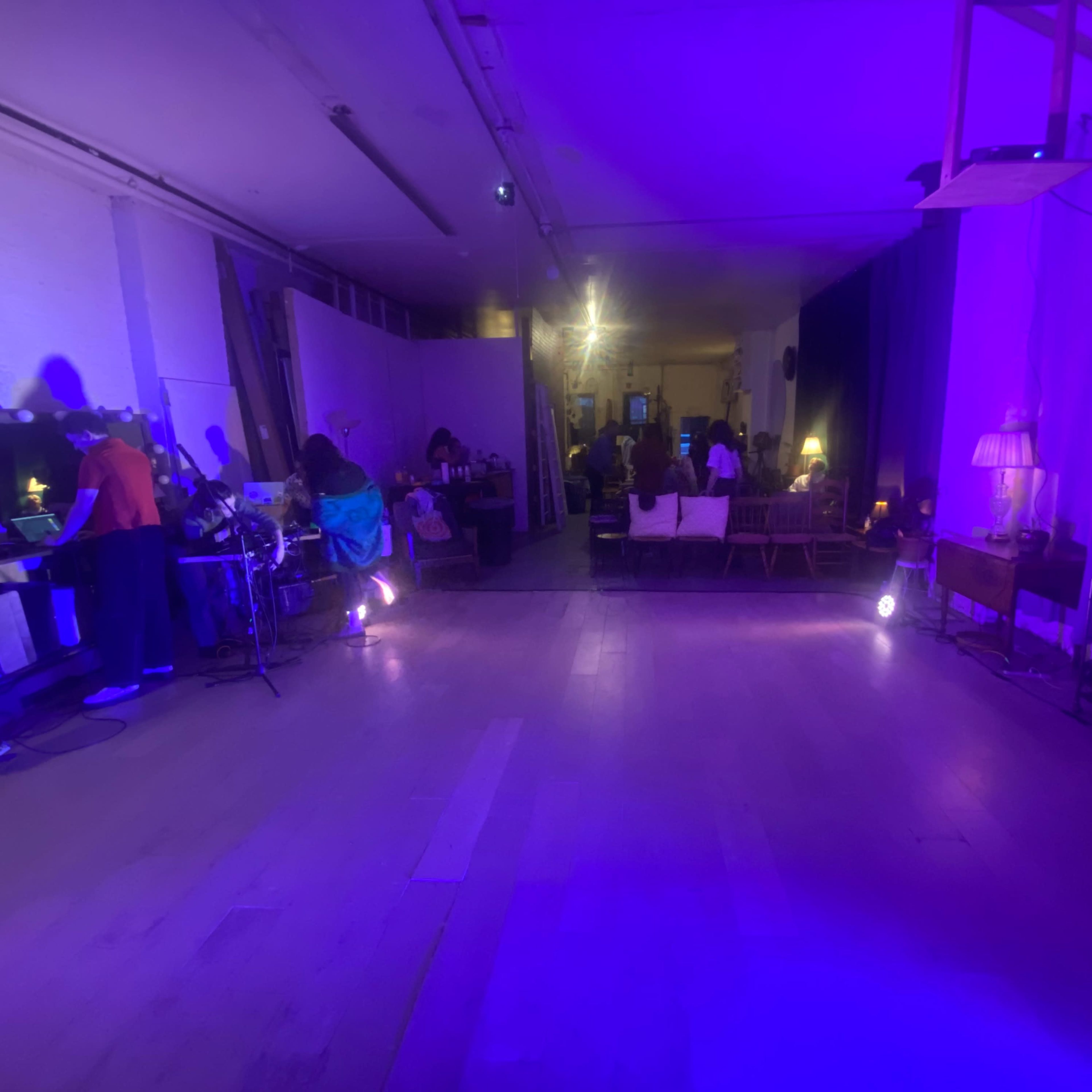 A spacious room with purple lighting, featuring various furniture pieces and people gathered in the background.