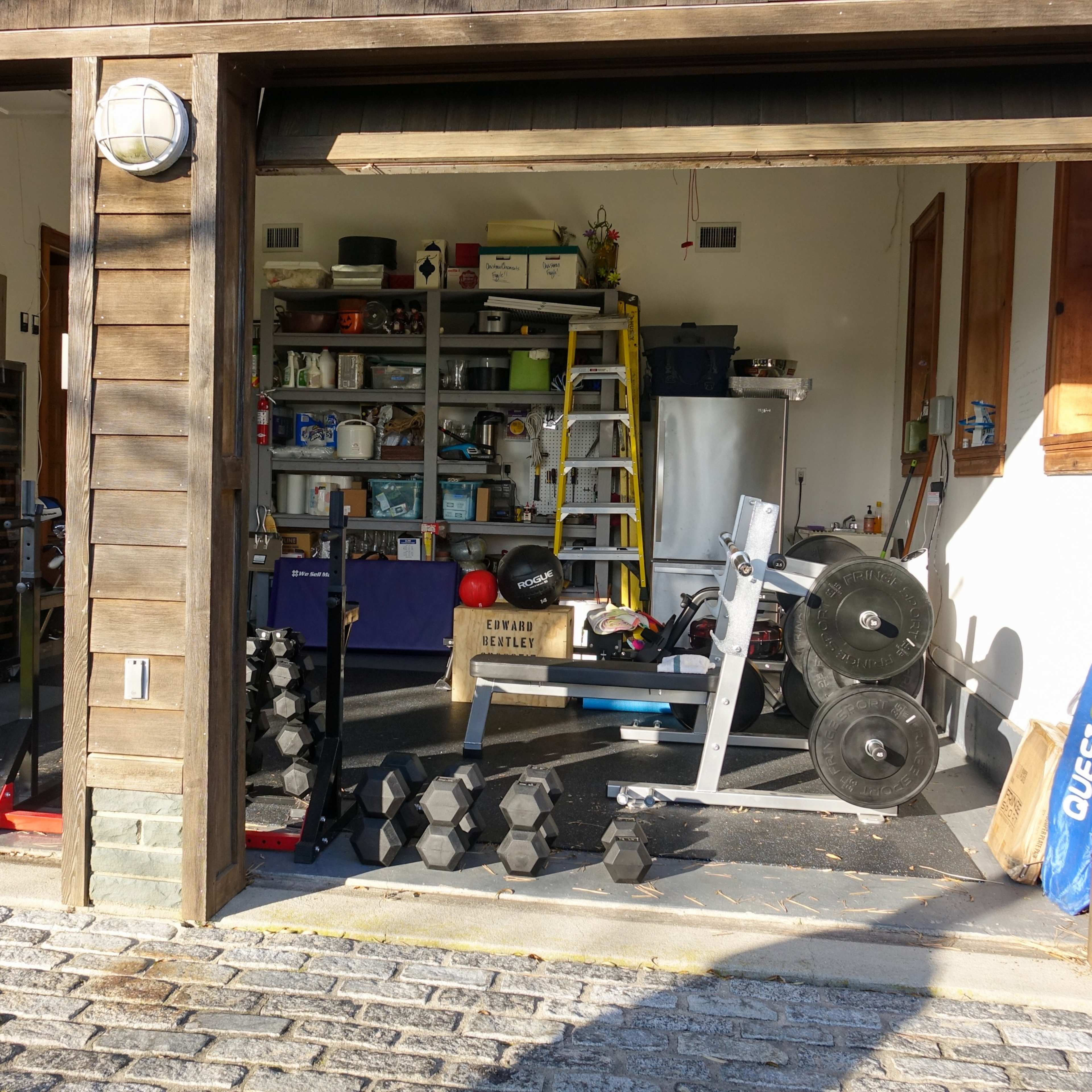 A garage with fitness equipment, including weights and a bench, alongside various storage items and tools.