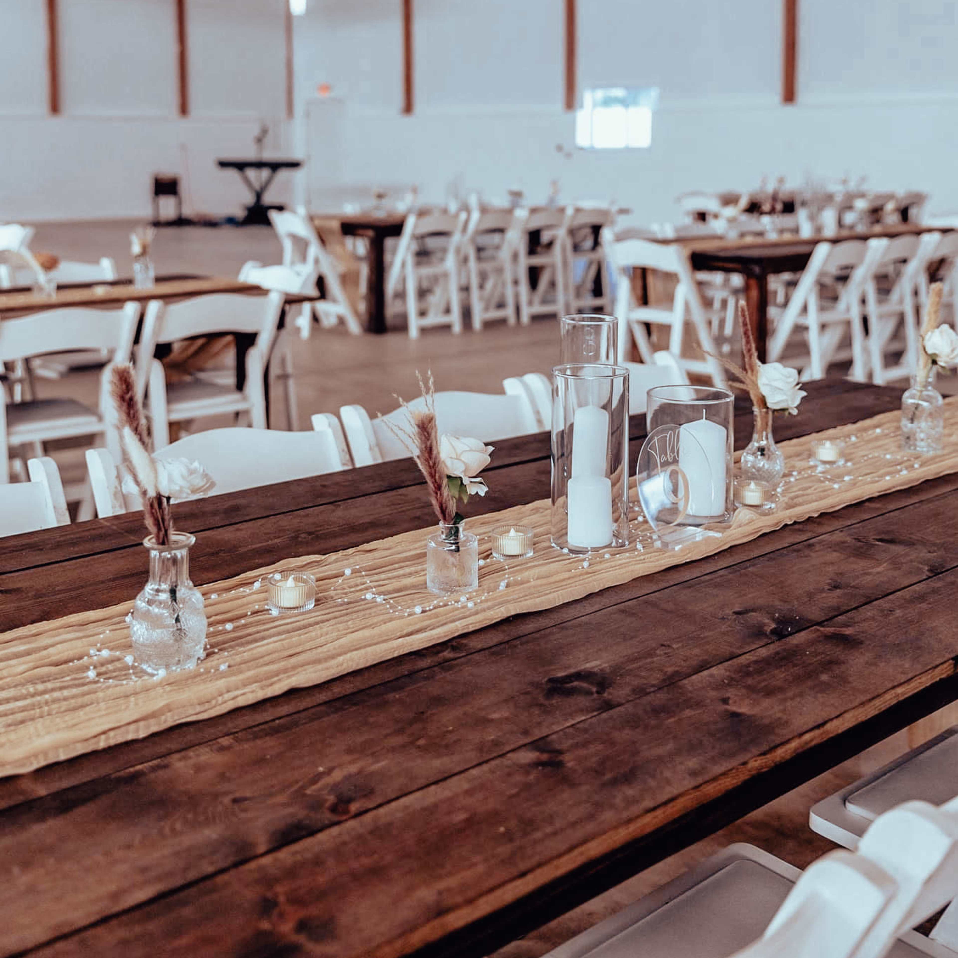 A spacious event hall features long wooden tables adorned with simple centerpieces and rustic table runners.